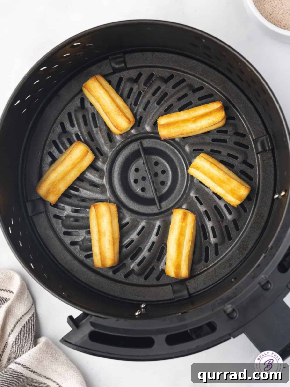 Golden perfection: Air Fryer Churro Bites cooking to crispy goodness Churro bites cooking in an air fryer basket, turning golden brown
