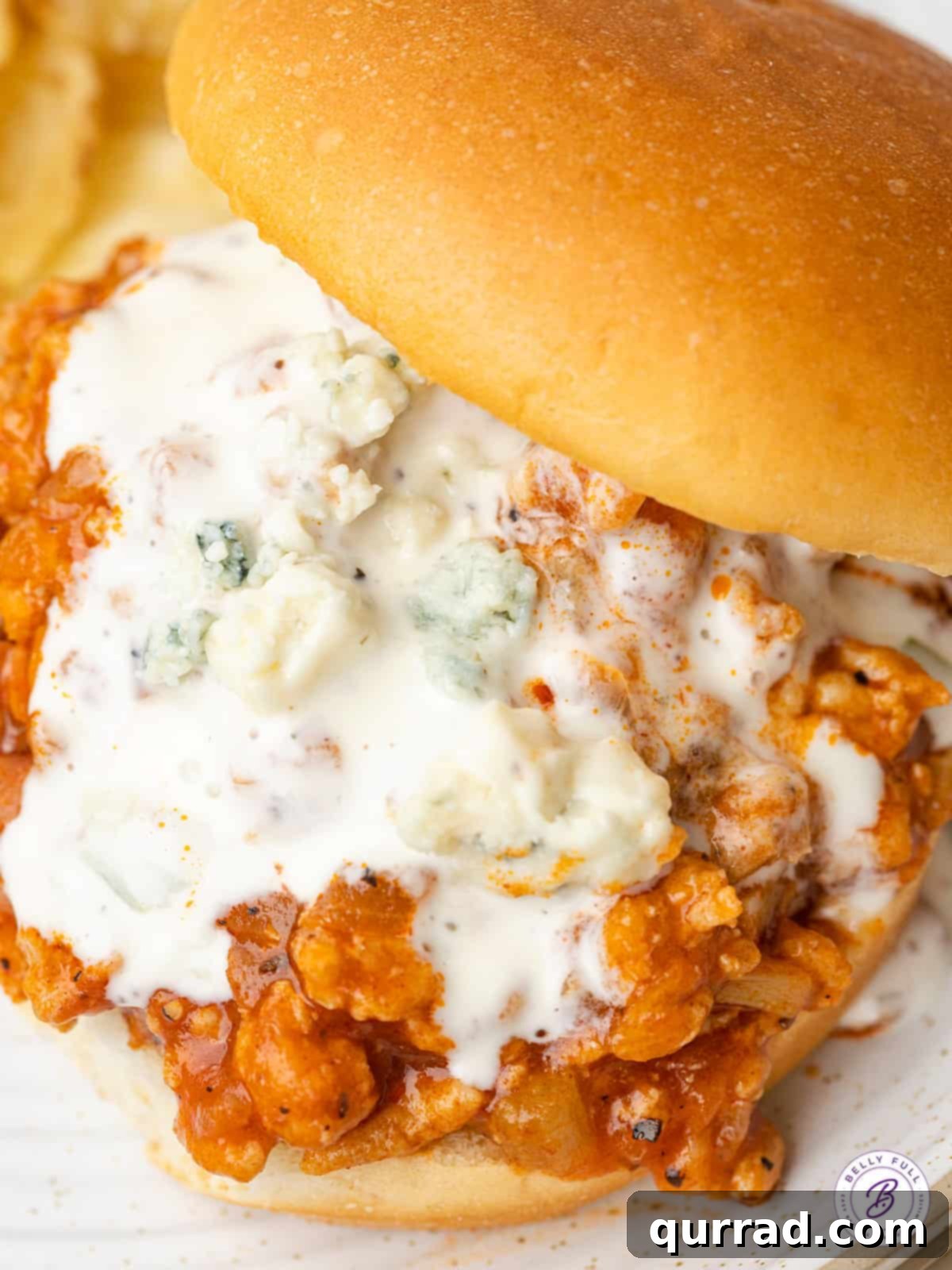 Buffalo Chicken Sandwich Mess 6 Close up of a prepared Buffalo chicken sloppy joe with blue cheese dressing on a toasted bun.