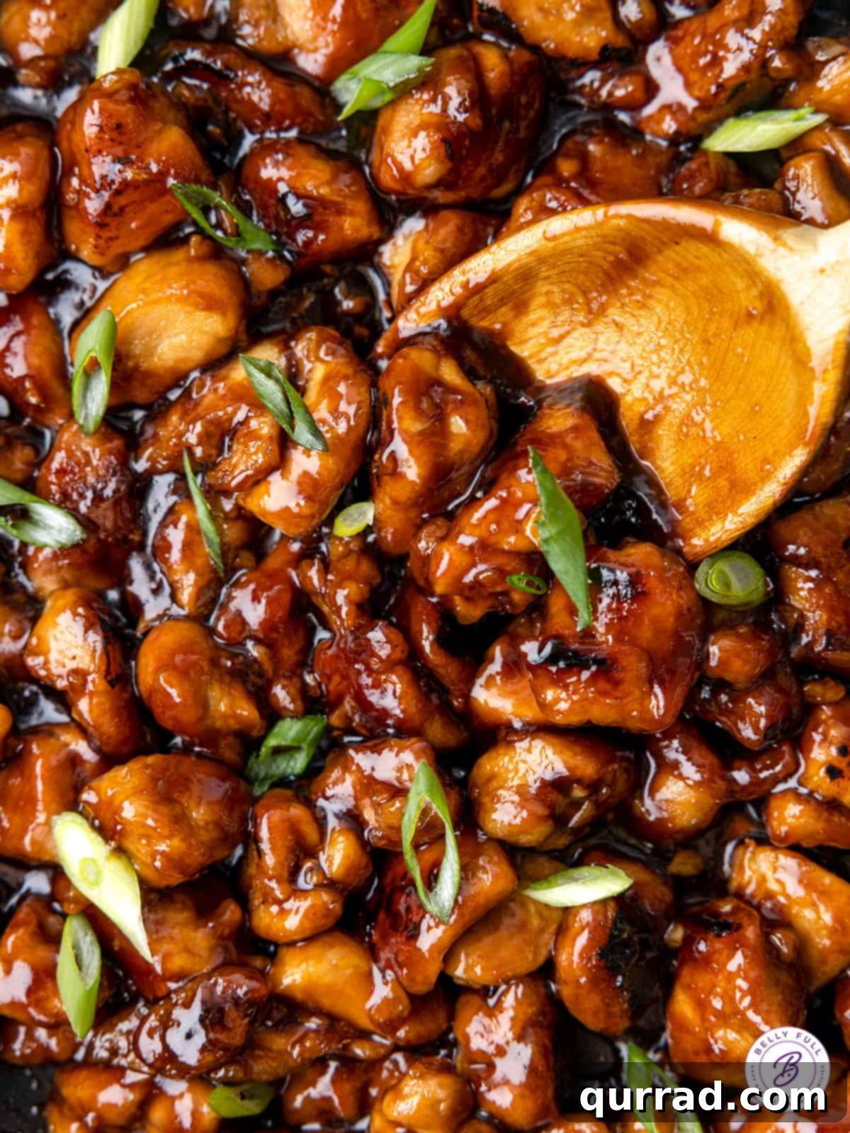 Homemade Bourbon Chicken: Better Than Takeout Flavor at Home A wooden spoon stirring homemade bourbon chicken in a pan, showcasing tender chicken pieces coated in a glistening, sticky-sweet sauce, ready to be served.