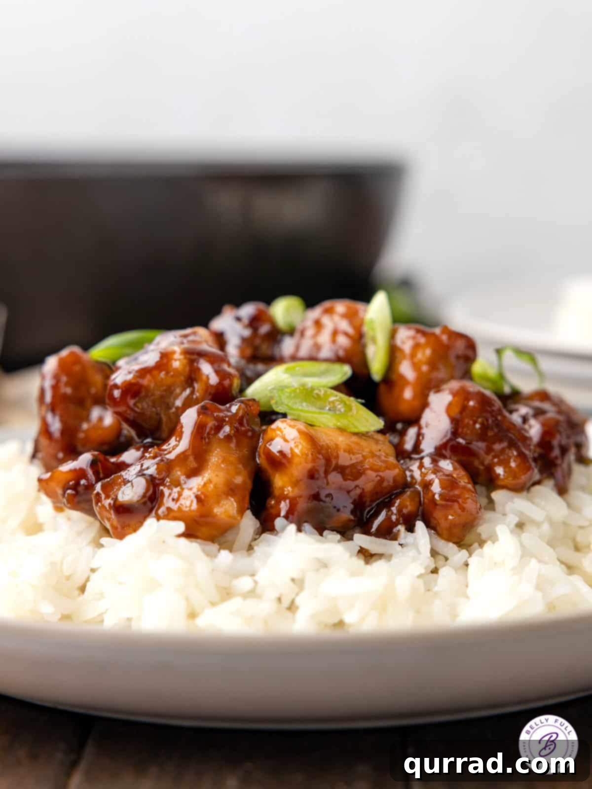 Delicious Bourbon Chicken Plated and Ready to Indulge In Side view of a serving plate filled with bourbon chicken and fluffy white rice, elegantly garnished with vibrant green onions, ready for a delicious meal.
