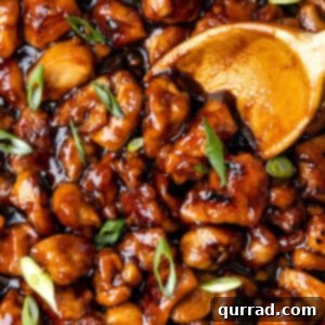 Sweet and Savory Bourbon Chicken 2 Homemade bourbon chicken in a pan being stirred with a wooden spoon, showcasing its rich, sticky sauce and tender chicken pieces.