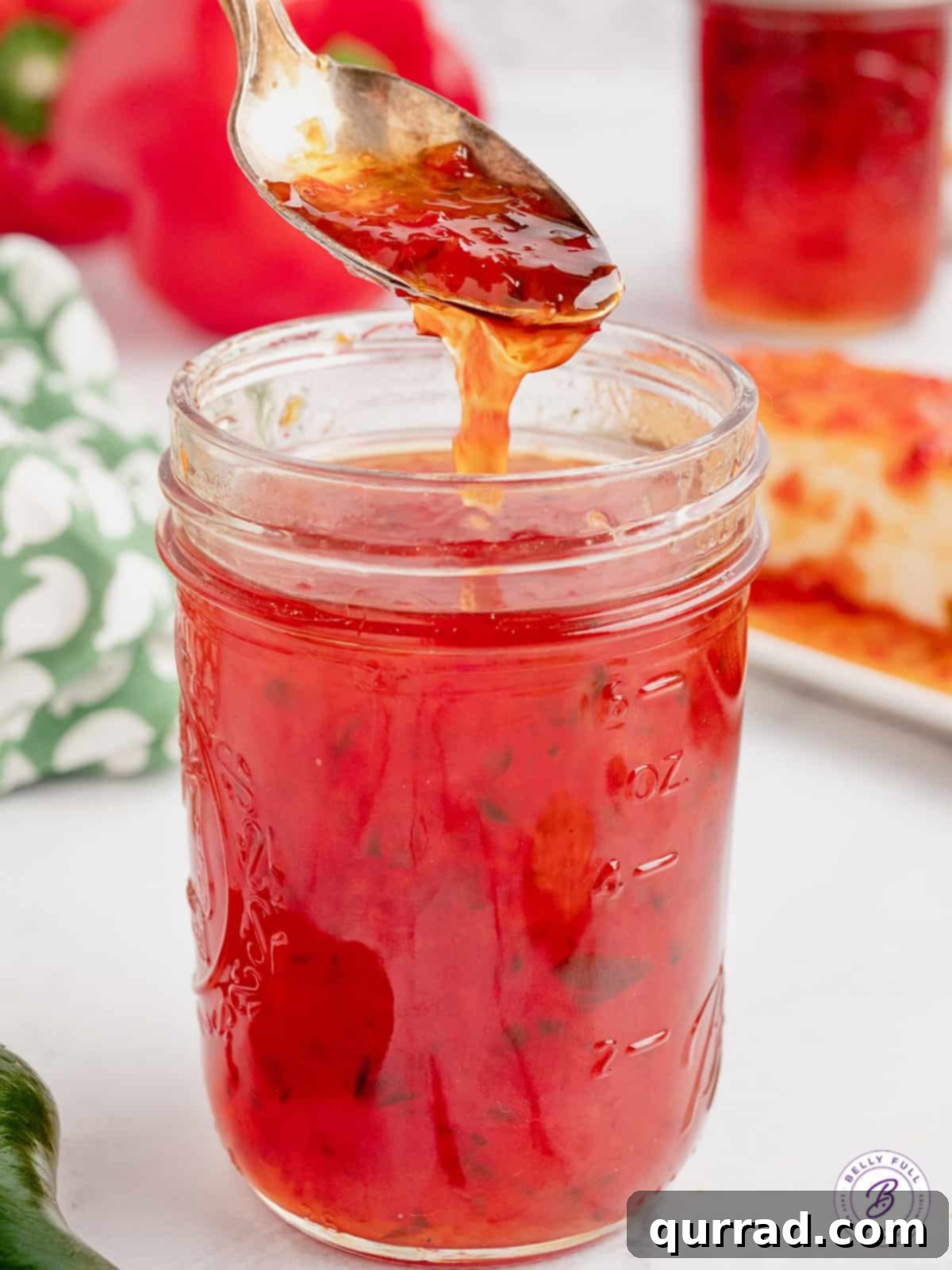 A spoon hovering over an open jar of red pepper jelly, ready to be served.