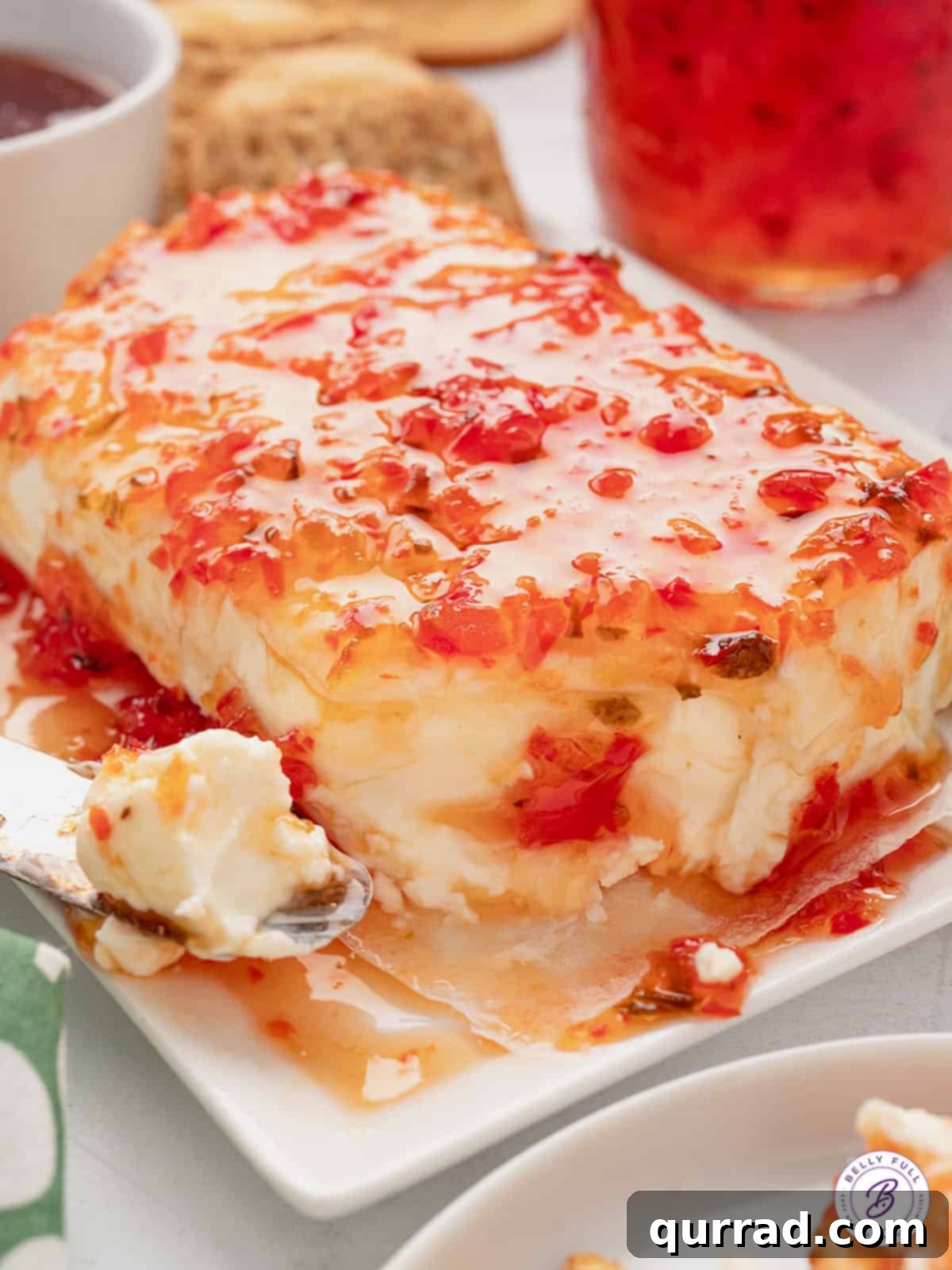 Red pepper jam elegantly spread over a block of cream cheese, ready for crackers.