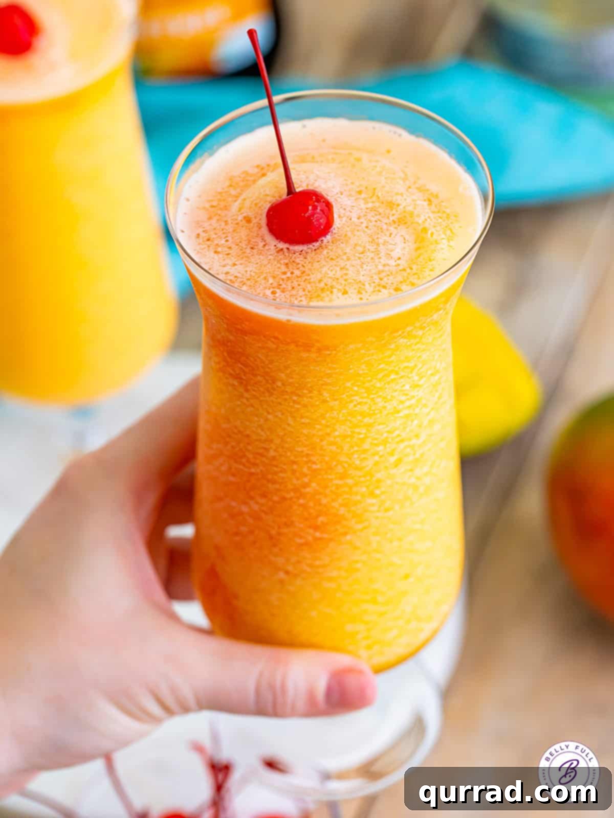 Enjoying a perfectly crafted Kiss on the Lips frozen cocktail. A hand holds a tall, elegant glass filled with a perfectly made Kiss on the Lips cocktail, garnished with a maraschino cherry. The drink's appealing colors and frosty texture are clearly visible, inviting a refreshing sip.
