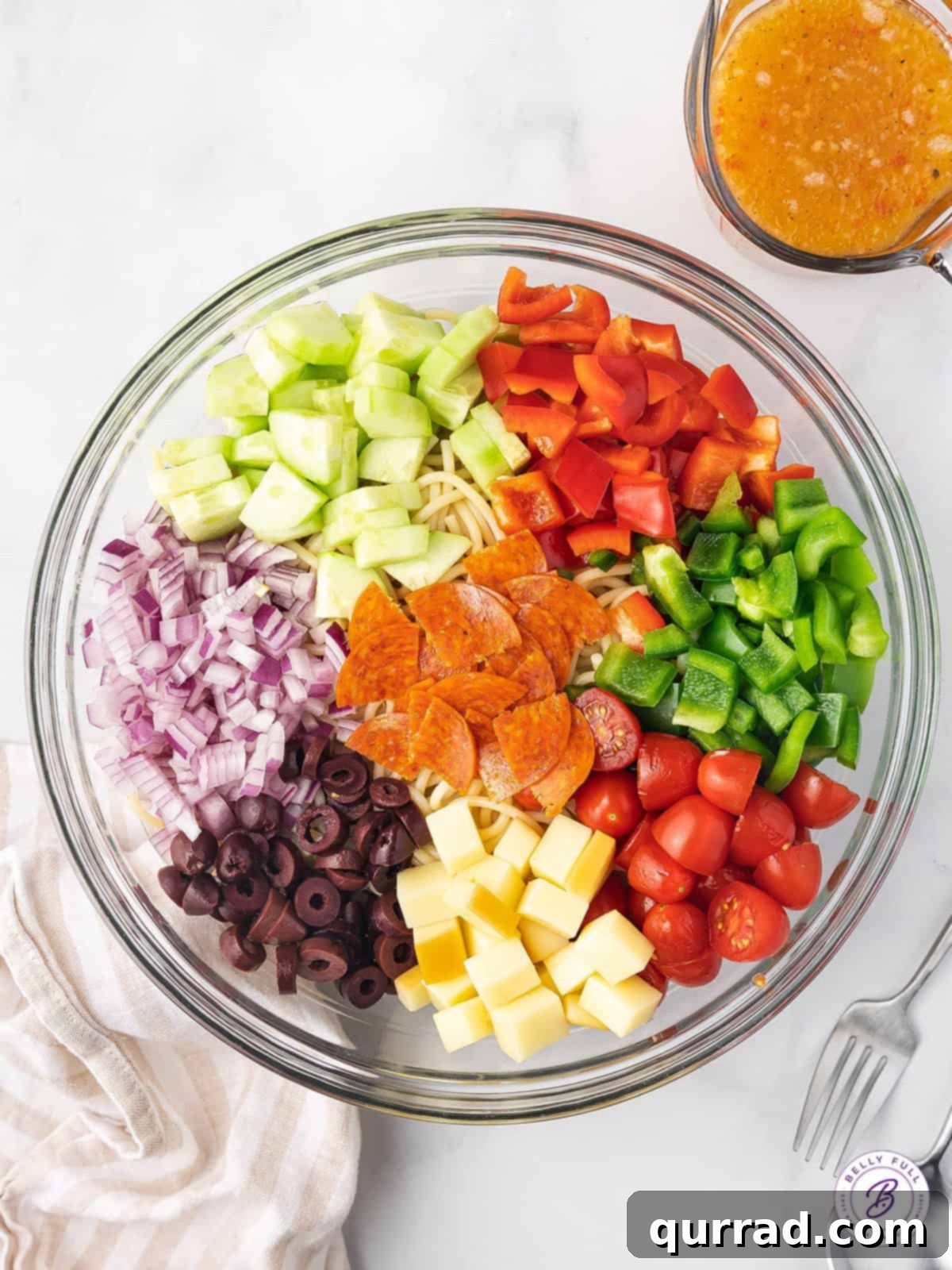Spaghetti Salad: Assembling fresh ingredients for a vibrant pasta dish. A large mixing bowl filled with raw ingredients for spaghetti salad: diced bell peppers, red onion, cucumber, pepperoni, provolone, olives, and grape tomatoes, ready for pasta.