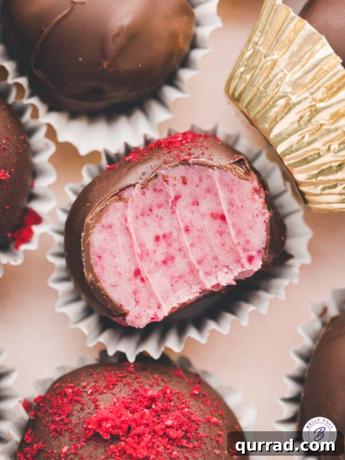 A chocolate covered raspberry truffle with a bite missing to show the inside