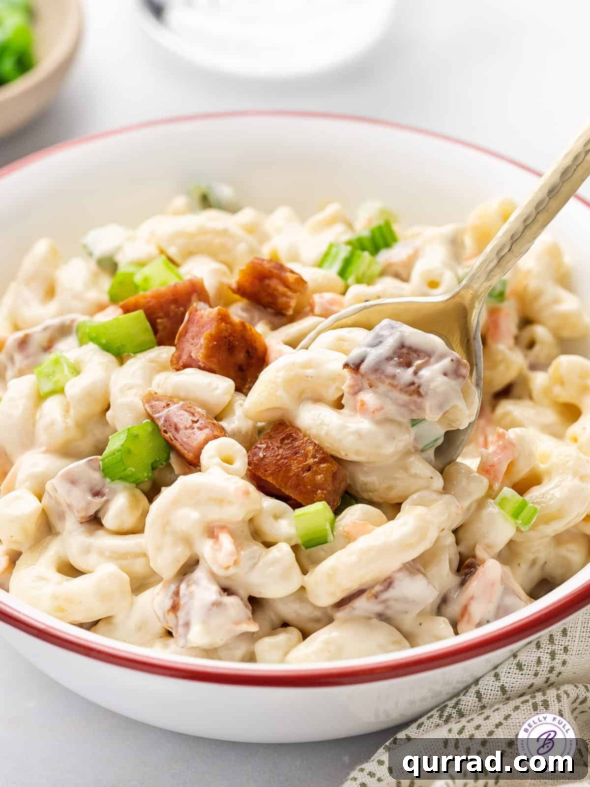 This Hawaiian Macaroni Salad recipe is made with grated carrot and onion, then coated in a creamy dressing that’s a bit tangy and sweet. A serving spoon lifting a generous portion of creamy Hawaiian macaroni salad from a large bowl, ready to be enjoyed