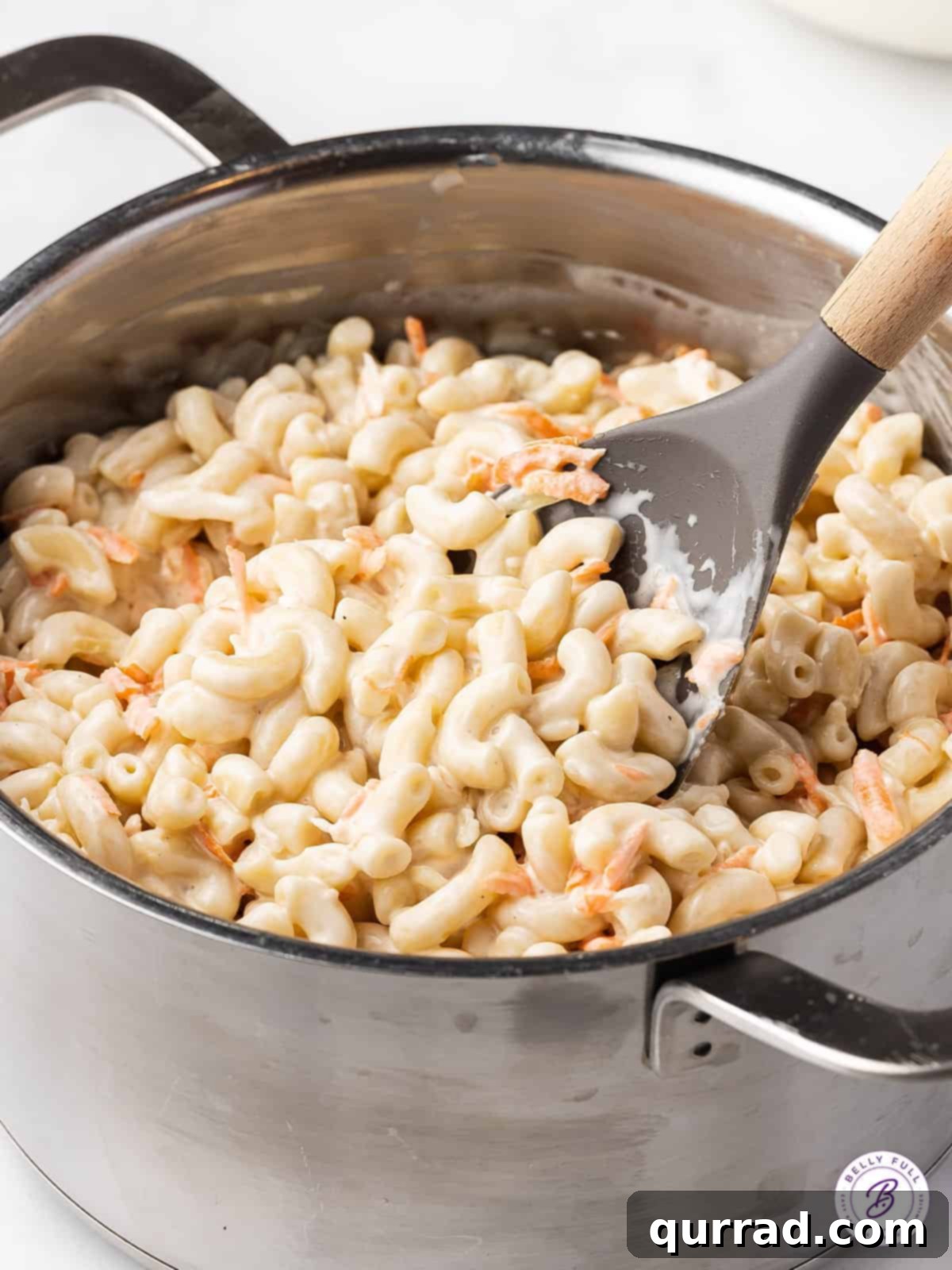 This Hawaiian Macaroni Salad recipe is made with grated carrot and onion, then coated in a creamy dressing that’s a bit tangy and sweet. A spoon gently stirring the creamy dressing into Hawaiian macaroni salad to ensure optimal flavor absorption and texture