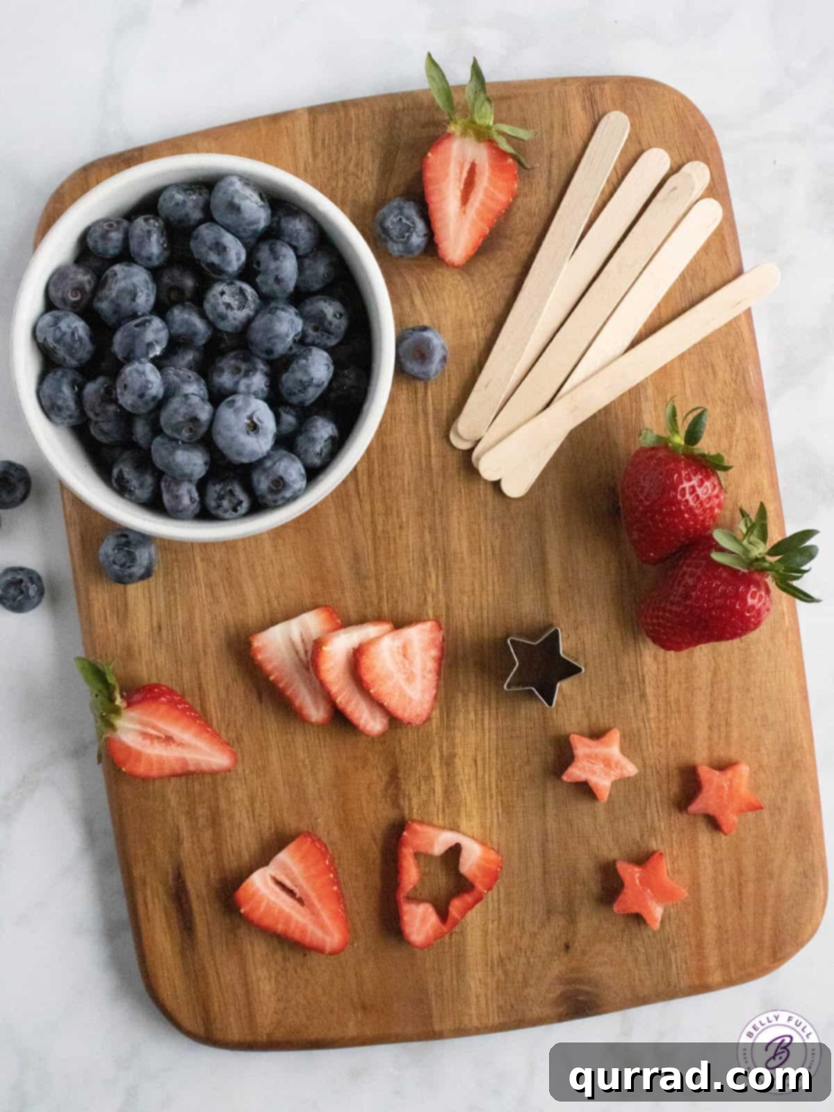 Overhead view of fresh ingredients for 4th of July popsicles: strawberries, blueberries, yogurt, cream, and maple syrup
