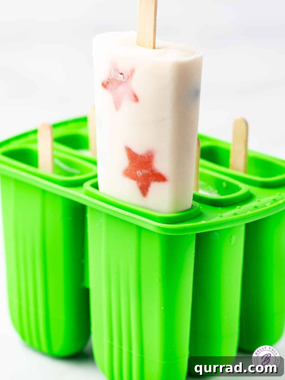 A vibrant red, white, and blue popsicle being gently pulled from a silicone mold, showcasing its perfect shape and layered fruit