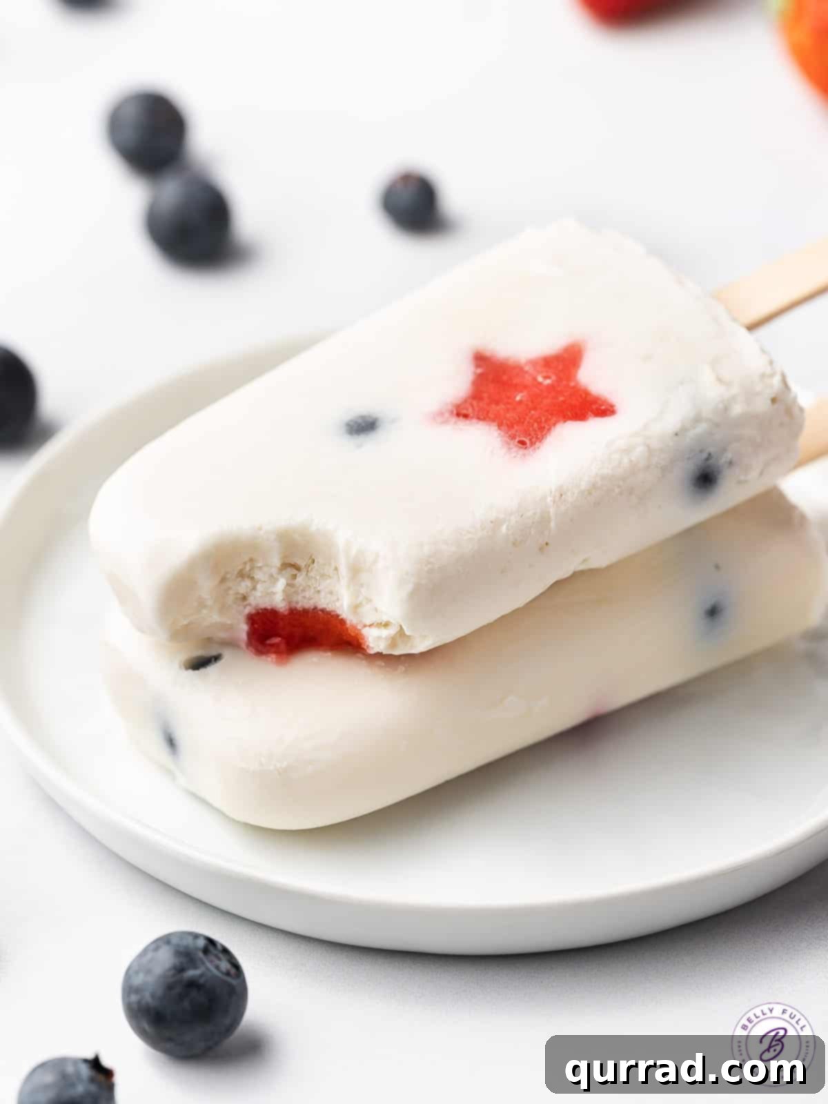 Two vibrant red, white, and blue popsicles stacked, one with a bite missing, showcasing the delicious layers and fruit