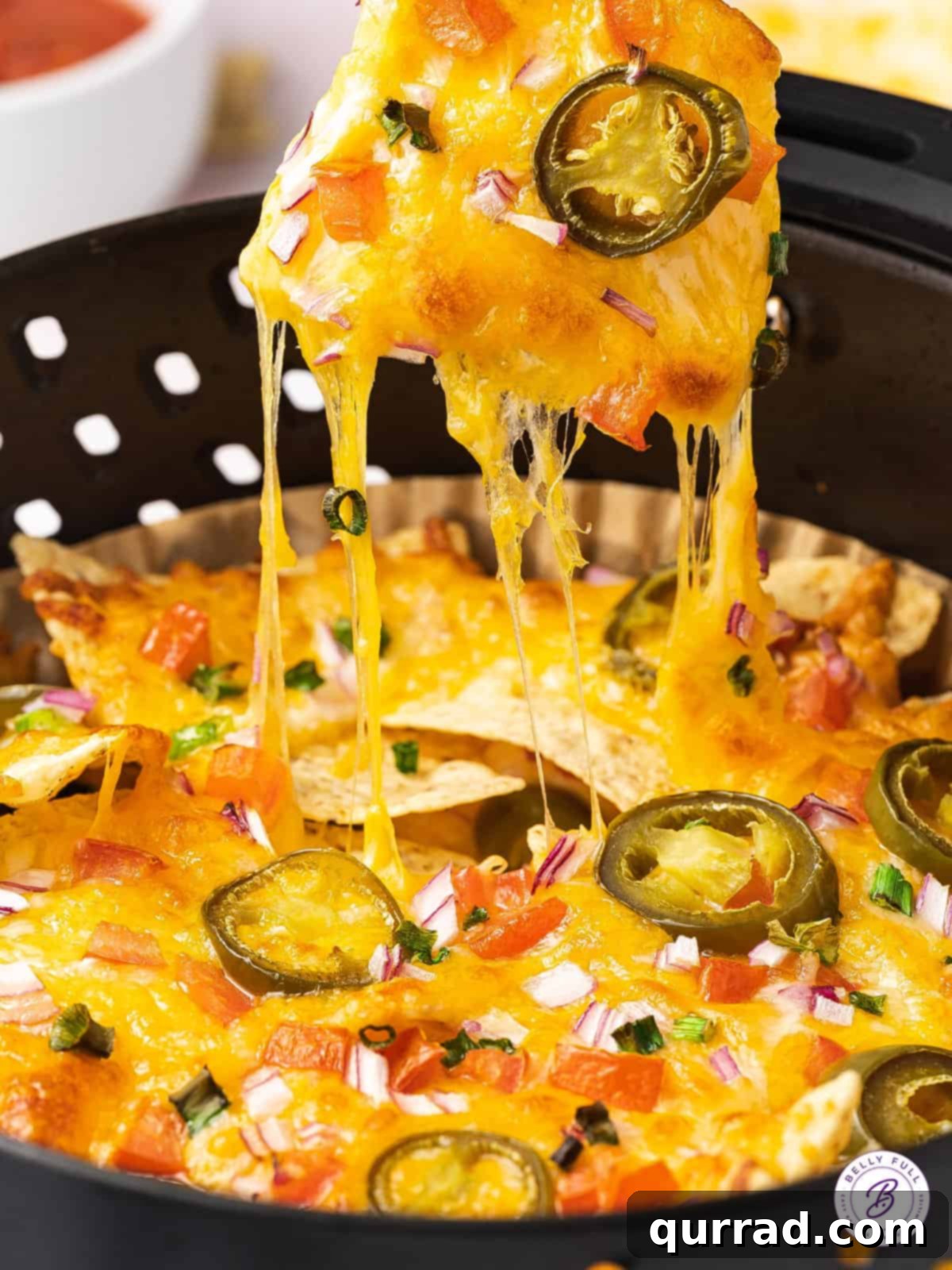 A hand pulling a single nacho from a basket of air-fried nachos, showing melted cheese and toppings.