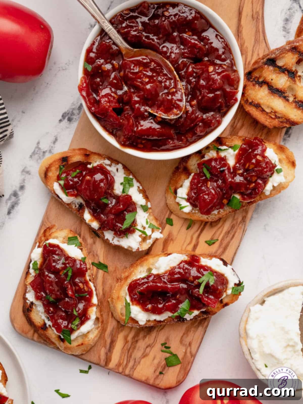 Overhead view of a jar of tomato jam next to slices of bread topped with cheese and tomato jam.