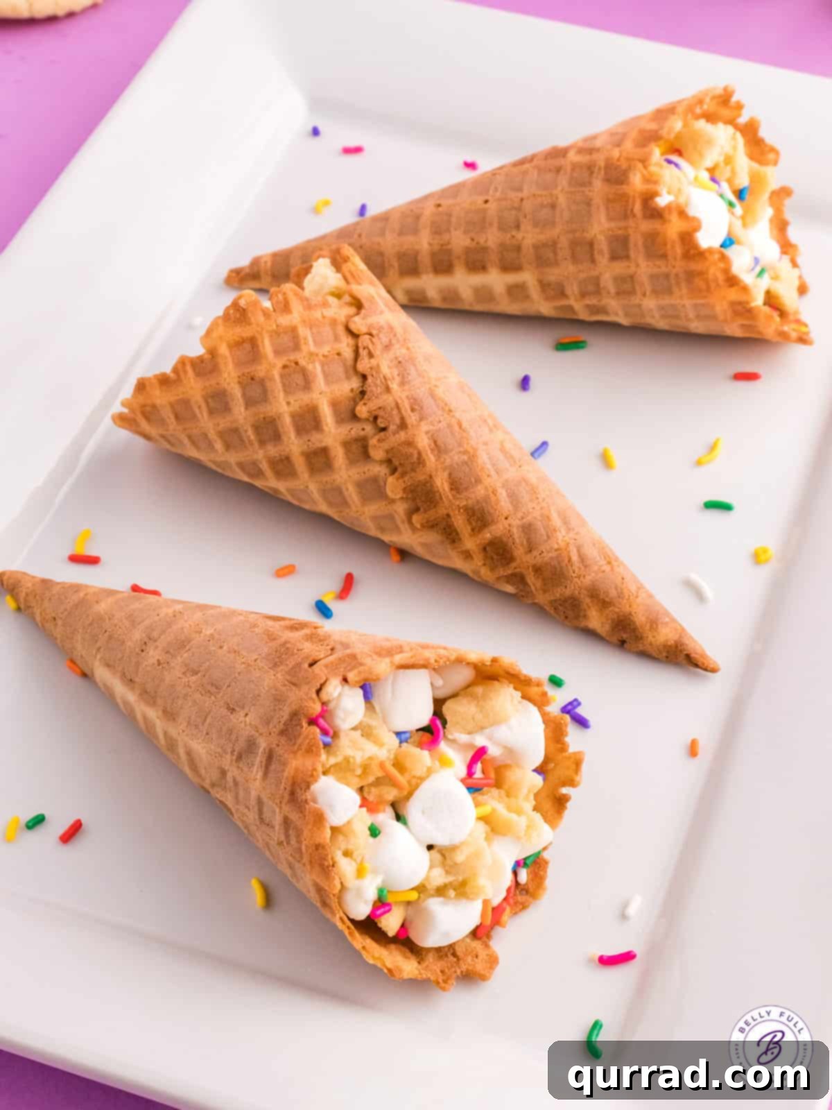 A trio of waffle cones stuffed with marshmallows, white chocolate chips, and sugar cookies, ready for a sweet treat! Overhead view of three perfectly cooked campfire cones on a white serving tray