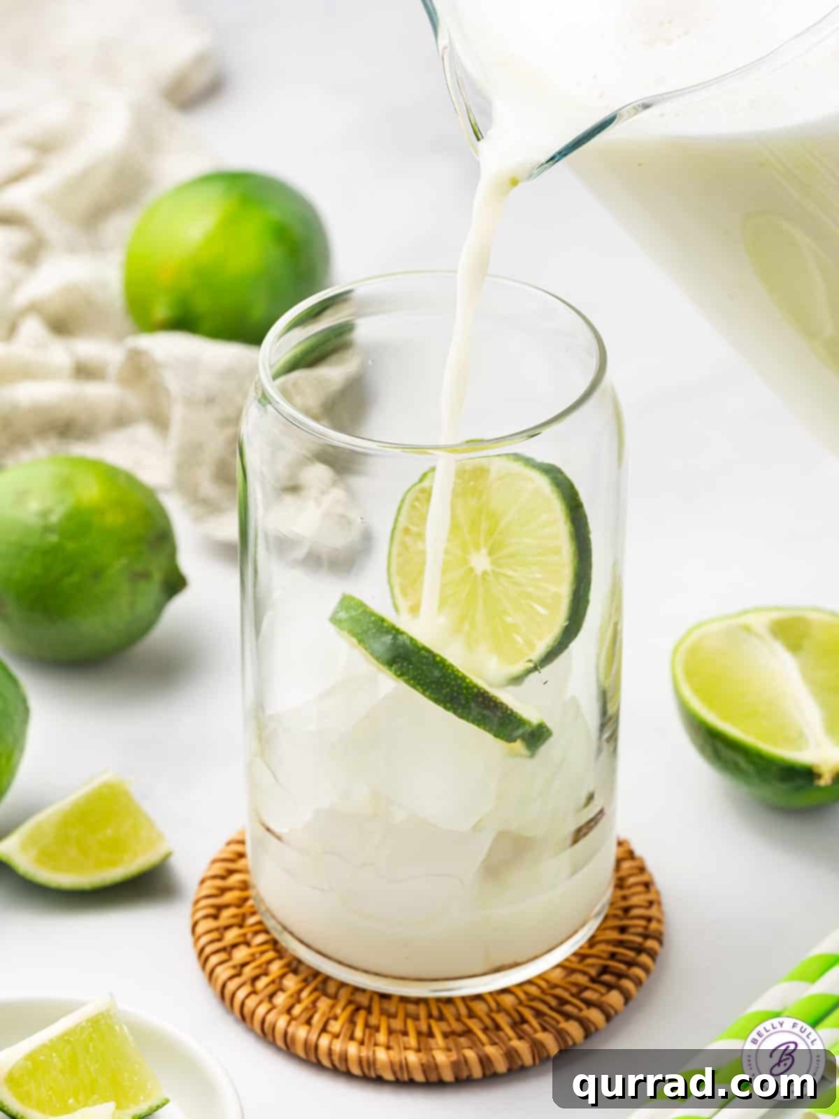 Watch the luscious Brazilian Lemonade pour, made with fresh lime juice, zest, and sweetened condensed milk, a truly refreshing experience. Brazilian lemonade being poured into a glass over ice, showing its creamy texture.