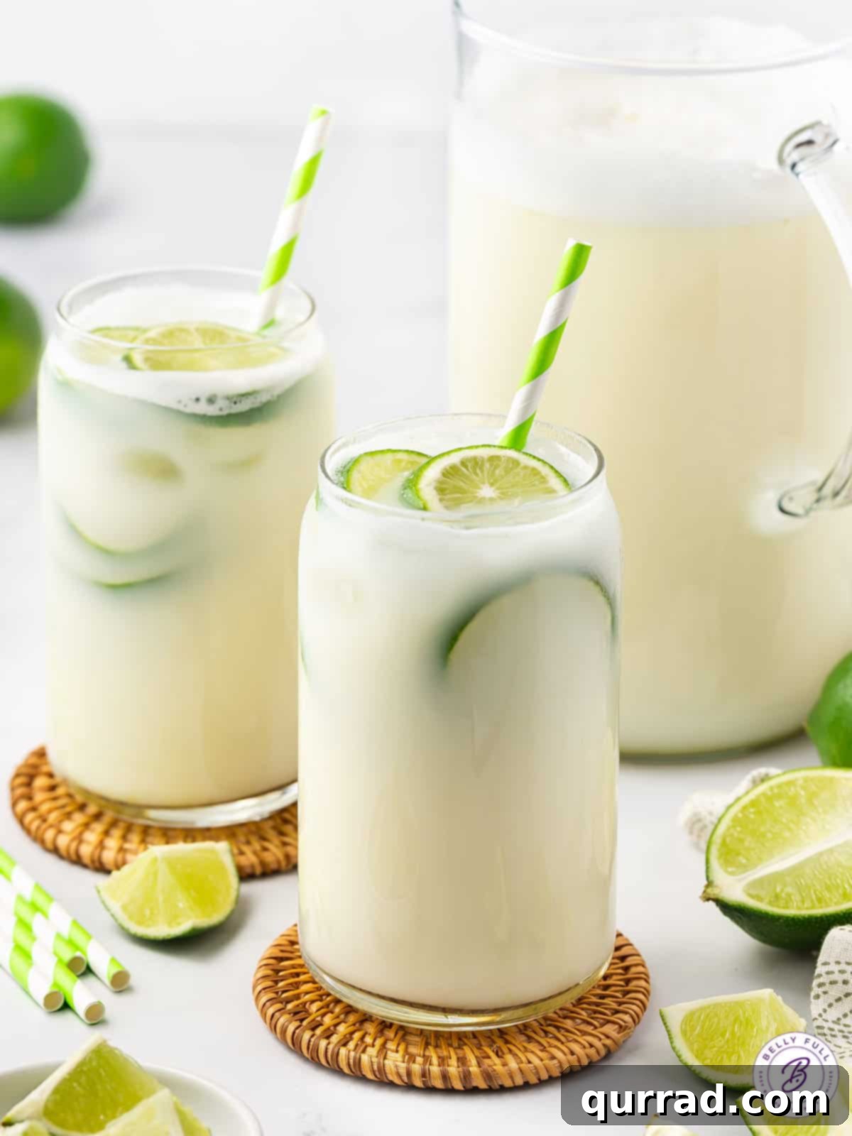 Enjoy two glasses of rich, luscious, and super refreshing Brazilian Lemonade, a perfect blend of fresh lime juice, lime zest, and sweetened condensed milk. Two glasses of Brazilian lemonade garnished with lime slices on a rustic wooden board, ready to serve.