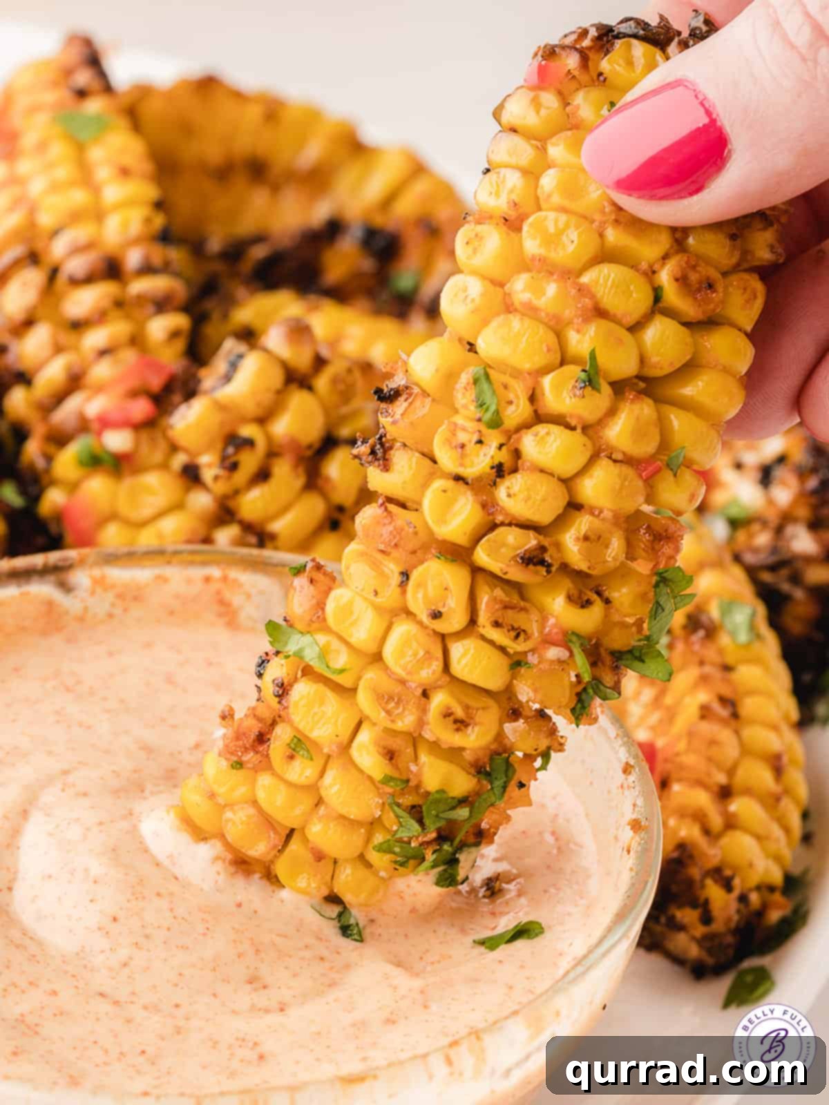 Addictive Air Fryer Corn Ribs 5 A hand dipping a corn rib into a creamy mayo dipping sauce, with more corn ribs in the background