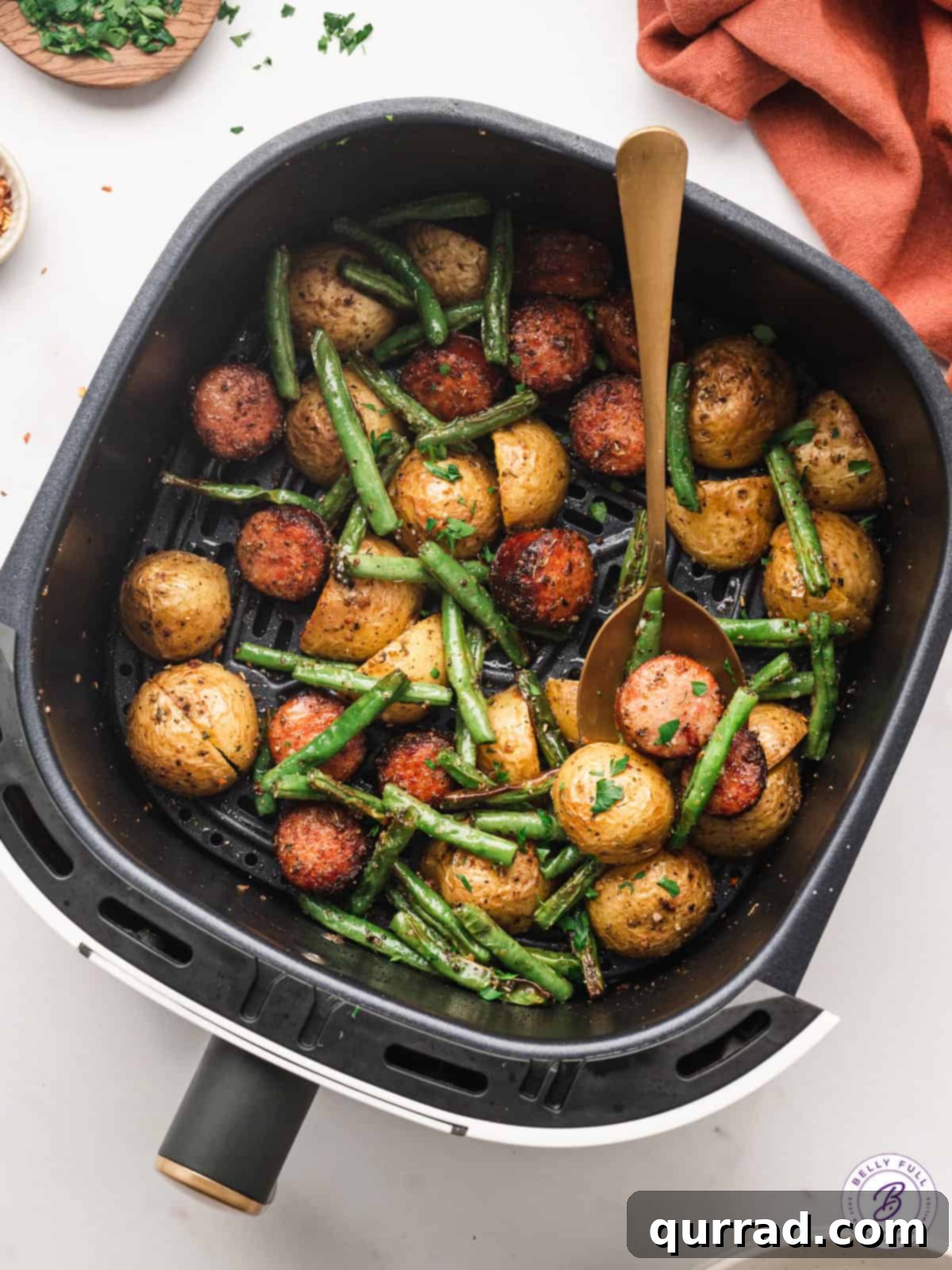 pieces of kielbasa, potatoes, and green beans in air fryer basket
