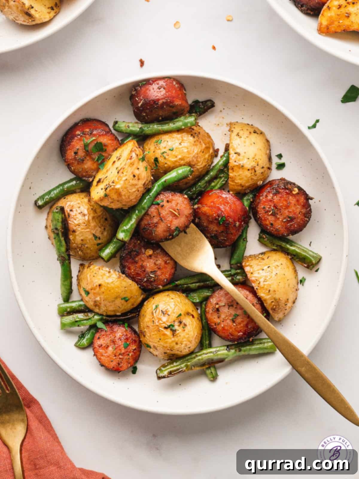 sliced roasted kielbasa, potatoes, and green beans on plate with fork