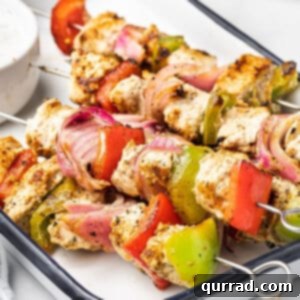 Close-up of freshly grilled Greek chicken kabobs on a white plate, showcasing the marinated chicken and colorful vegetables.