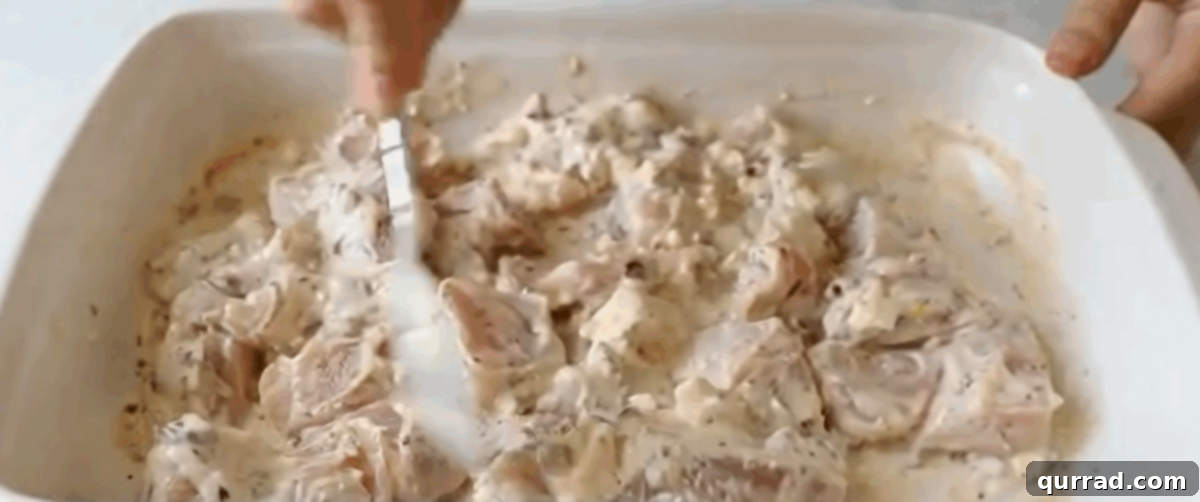 Chicken pieces marinating in a creamy Greek yogurt sauce with herbs and feta in a shallow dish, ready for refrigeration.