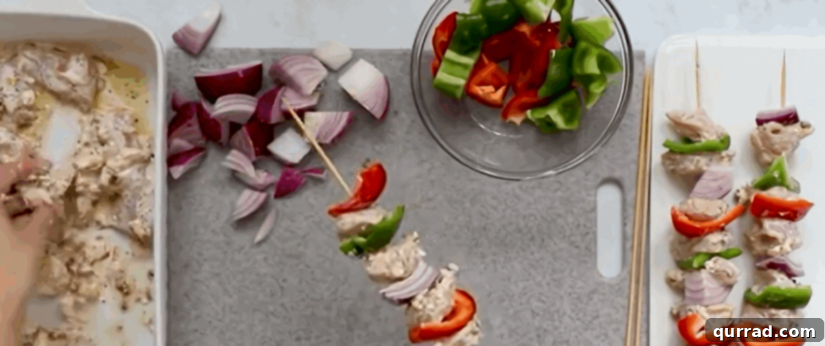 Hands carefully threading marinated chicken, vibrant red onion wedges, and colorful bell pepper pieces onto gleaming metal skewers, showcasing the assembly process.