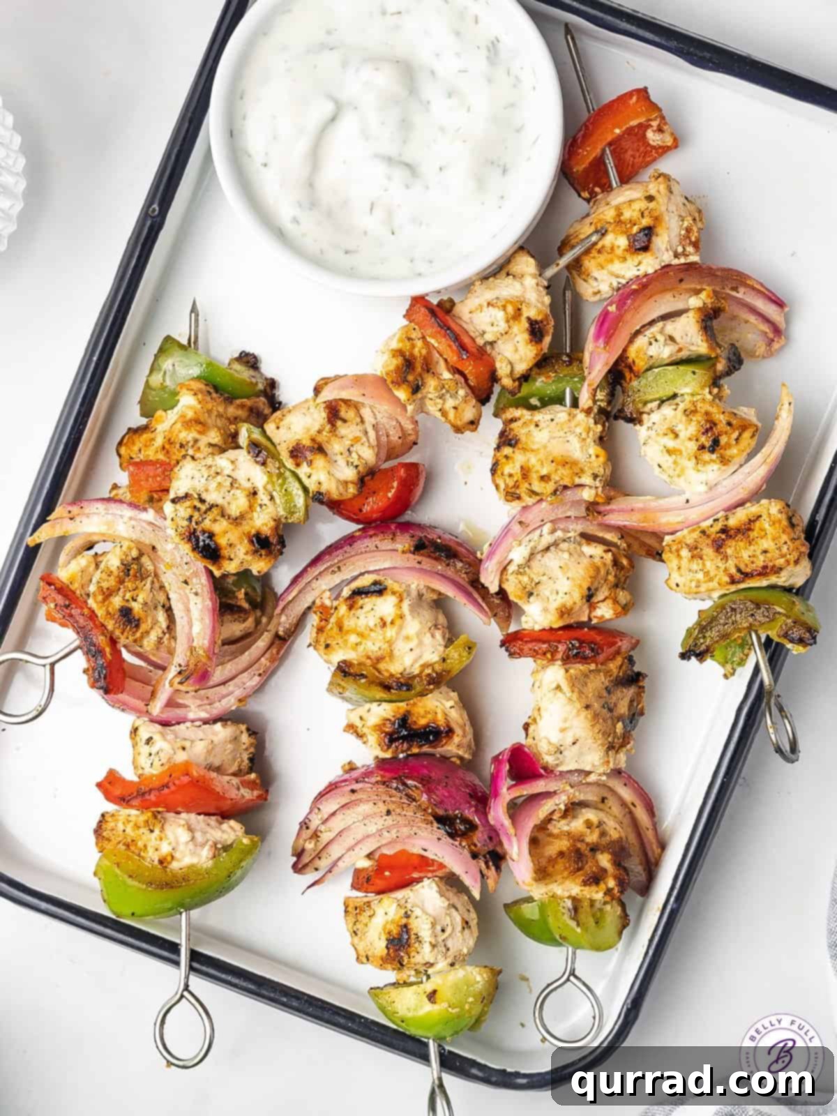 Perfectly grilled Greek chicken kabobs adorned with fresh parsley, served on a white platter alongside a bowl of creamy tzatziki sauce, ready for a delicious meal.
