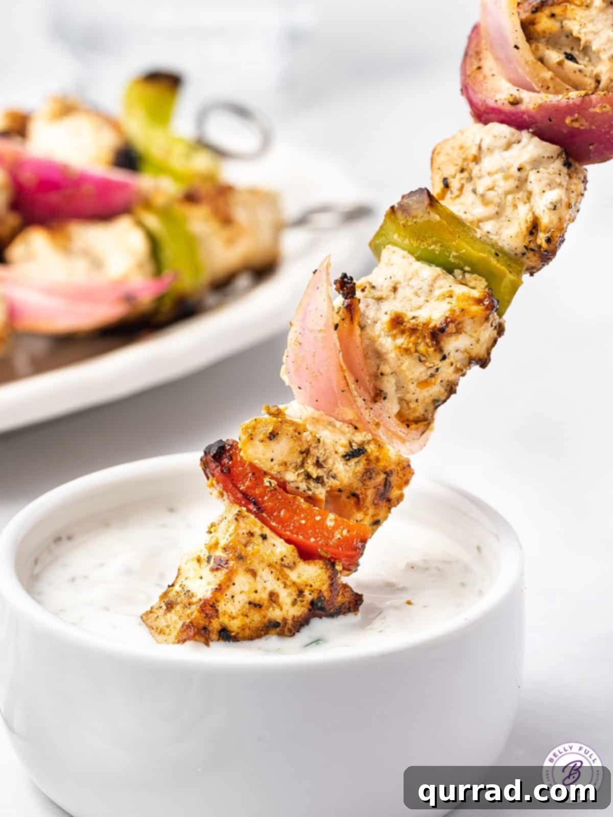 A vibrant Greek chicken skewer being gracefully dipped into a bowl of cool, creamy tzatziki sauce, highlighting the perfect pairing.