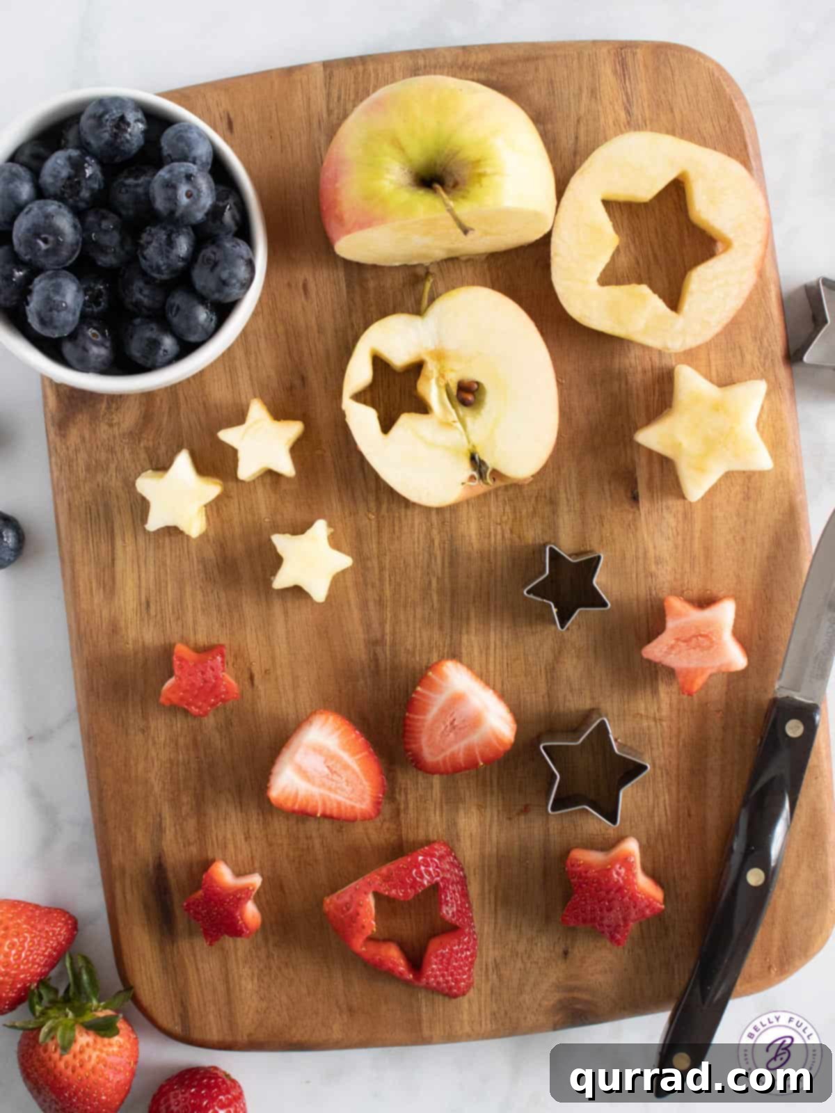 Tricolor Fruit Delights 3 Overhead view of 4th of July fruit kabob ingredients including whole strawberries, apples, blueberries, cookie cutters, and wooden toothpicks.