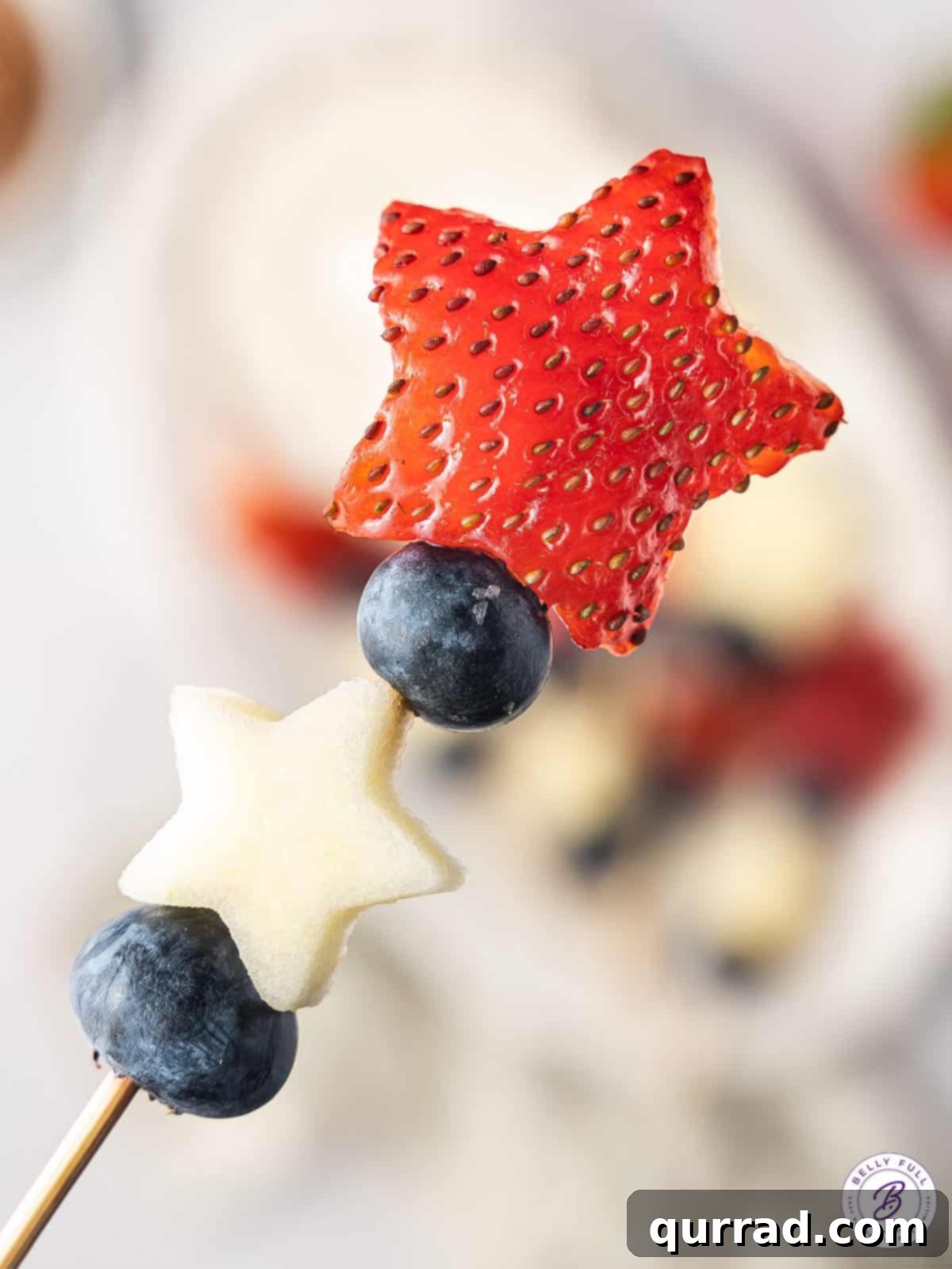 Tricolor Fruit Delights 4 Close up view of a red white and blue fruit skewer, featuring a strawberry star, apple star, and blueberries on a toothpick.