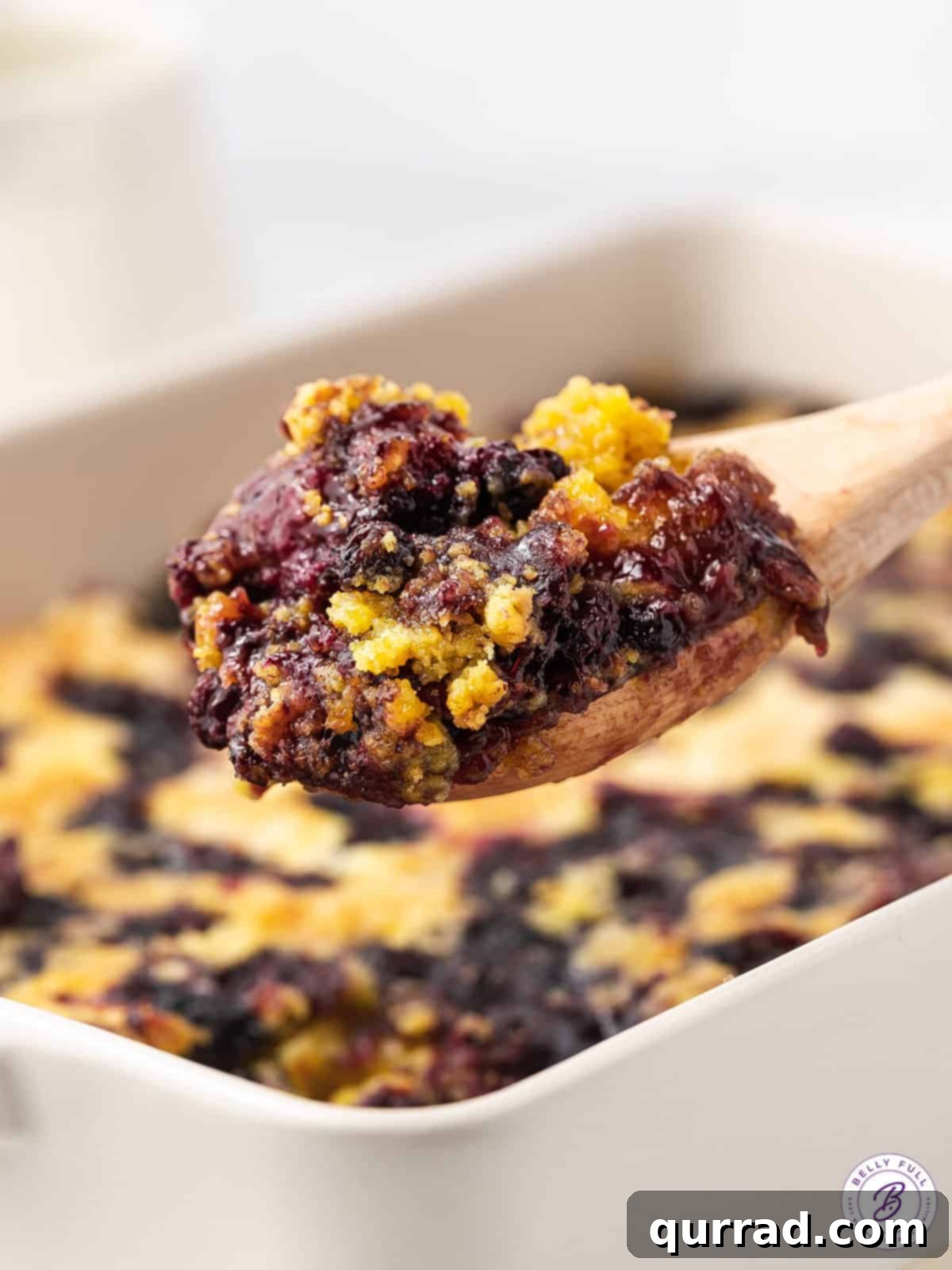 One Pan Blueberry Bliss 9 A scoop of freshly baked blueberry dump cake rests on a wooden spoon, showcasing its tender texture.