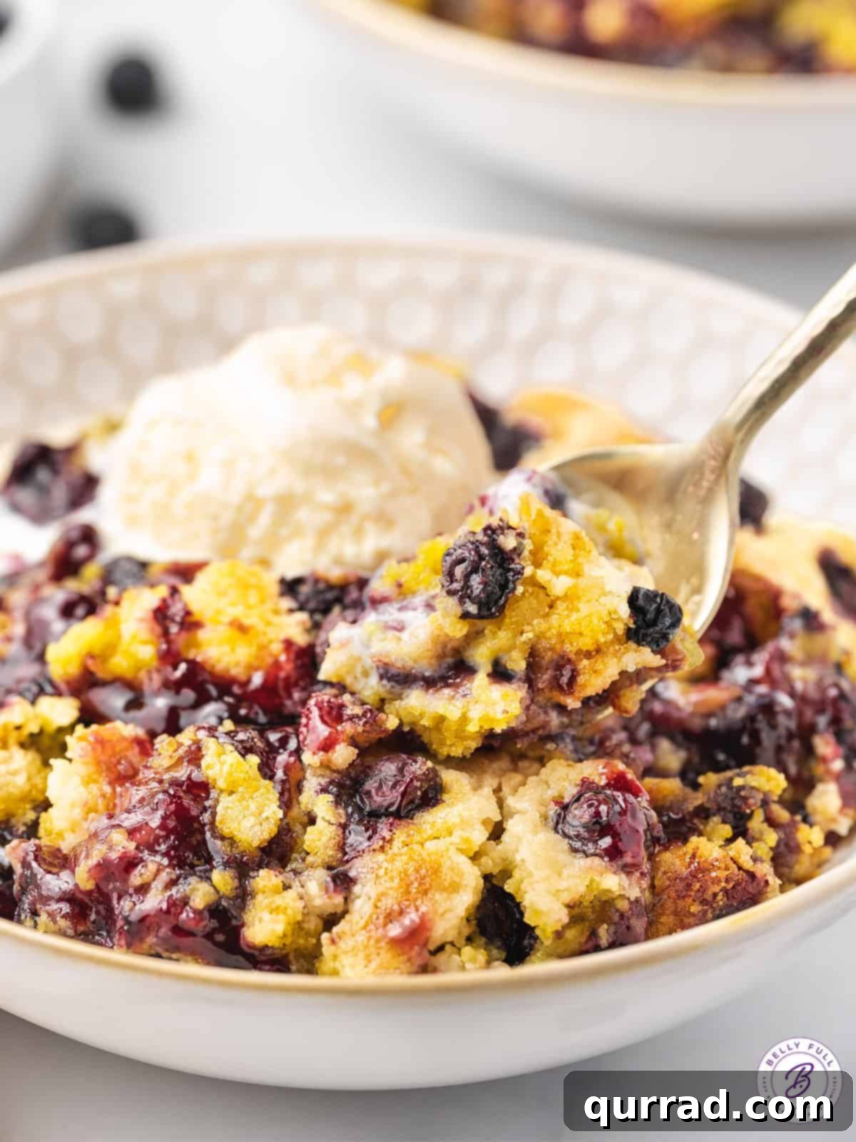 One Pan Blueberry Bliss 10 A close-up of a spoonful of warm blueberry dump cake topped with a scoop of melting vanilla ice cream.