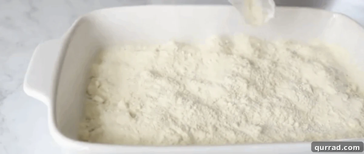 One Pan Blueberry Bliss 5 Dry lemon cake mix being sprinkled evenly over the blueberry pie filling in a baking dish.