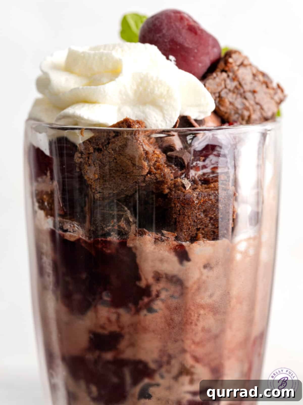 Decadent Black Forest Brownie Sundae with Whipped Cream Close-up view of a single Black Forest brownie sundae, generously topped with swirling whipped cream and a glistening red cherry.