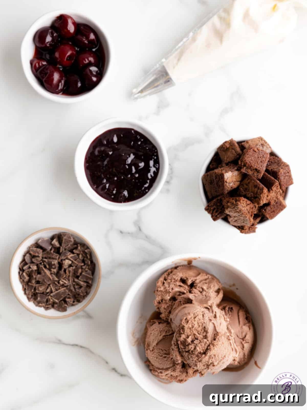 Essential Ingredients for Your Black Forest Sundae Individual ingredients for a Black Forest sundae laid out on a surface: cherry preserves, frozen cherries, chocolate ice cream, cubed brownies, and chopped dark chocolate.