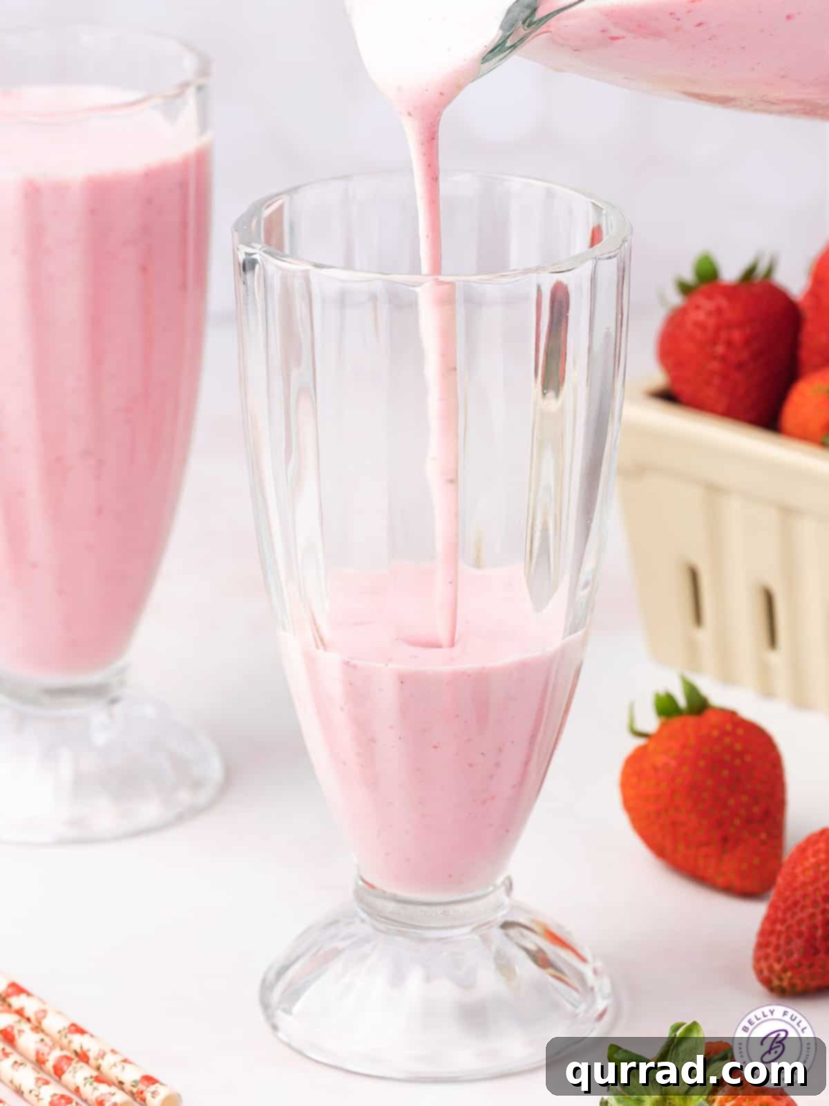 The perfect pour: Creating your Boozy Strawberry Shortcake Milkshake. A stream of rich, pink boozy strawberry milkshake being poured into a tall glass, indicating its creamy consistency and deliciousness.