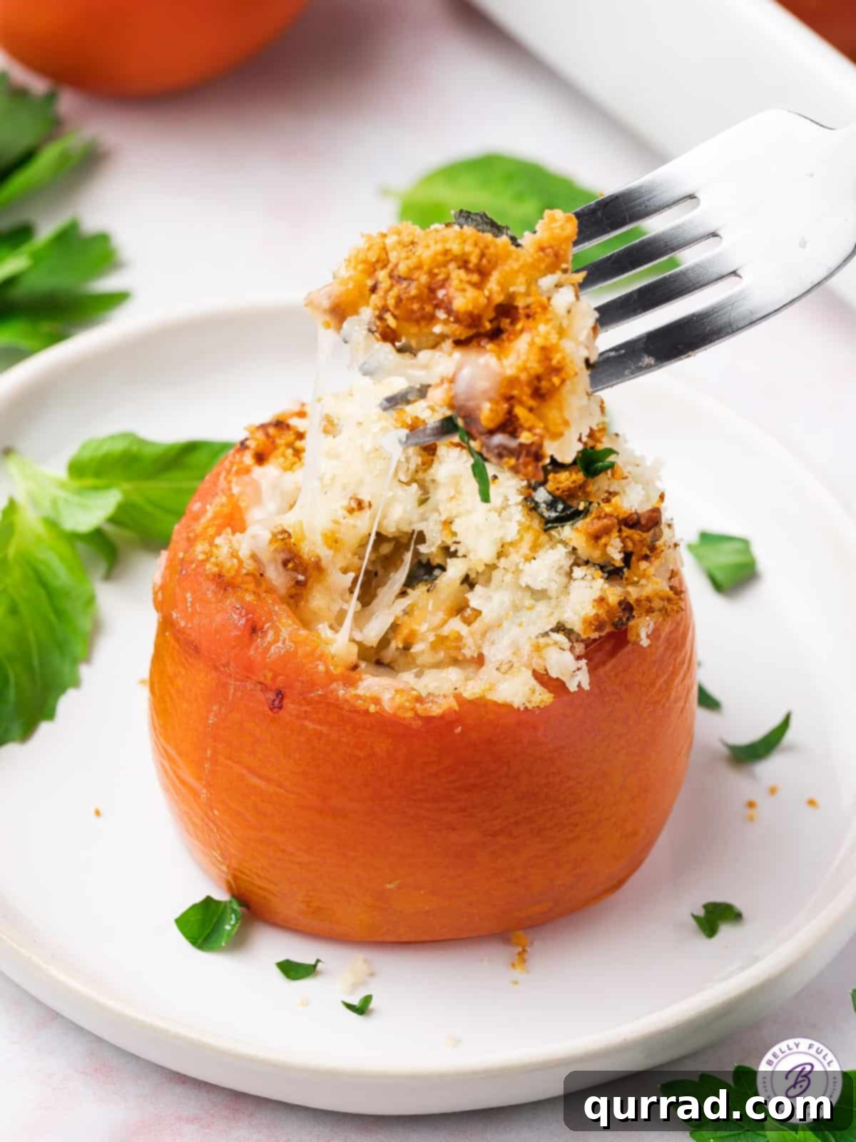 Close up shot of a fork lifting cheese and breadcrumbs from a whole stuffed tomato, highlighting the texture.