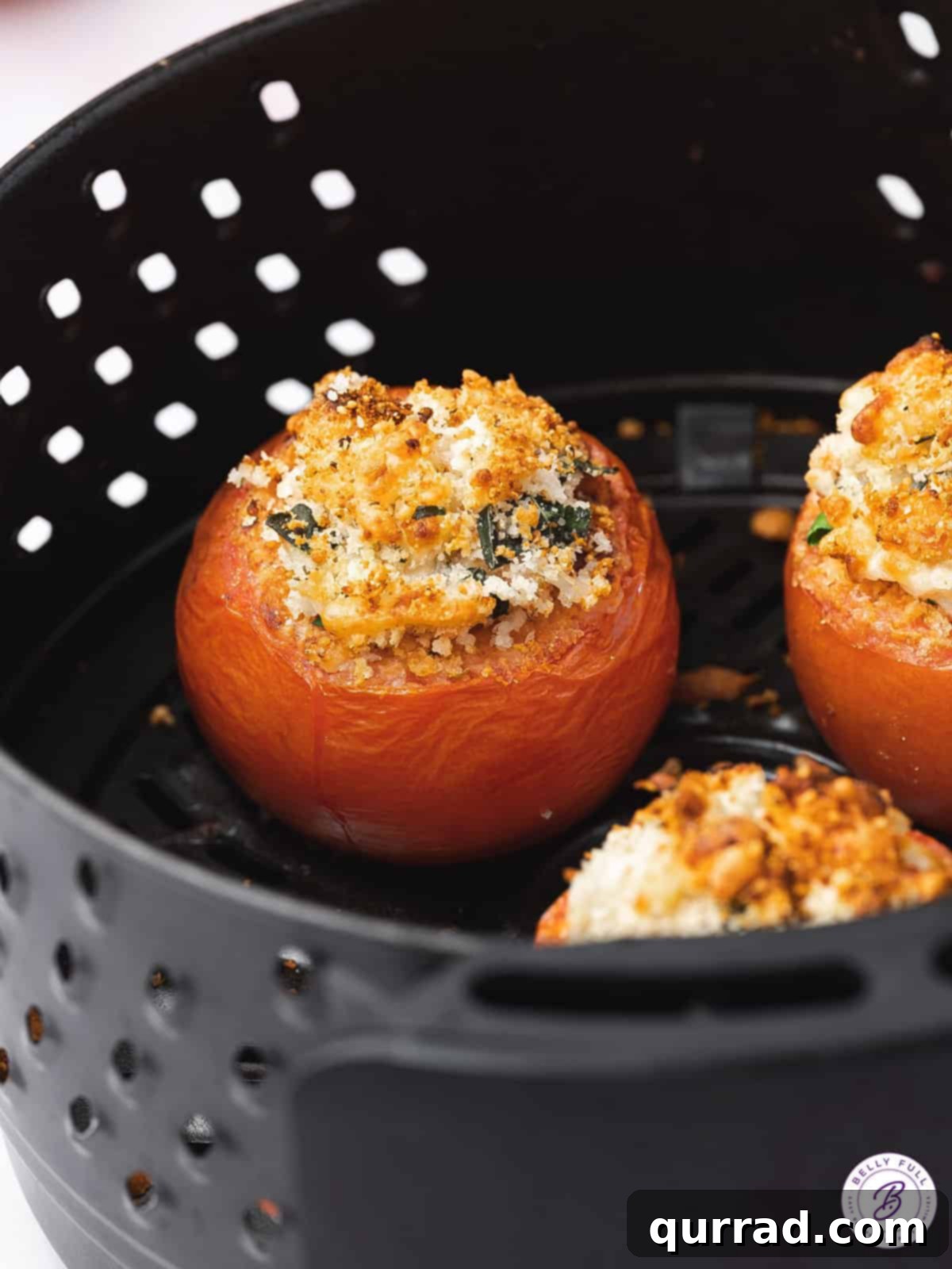 Stuffed whole tomatoes cooking in an air fryer basket, showing a golden, bubbly topping.