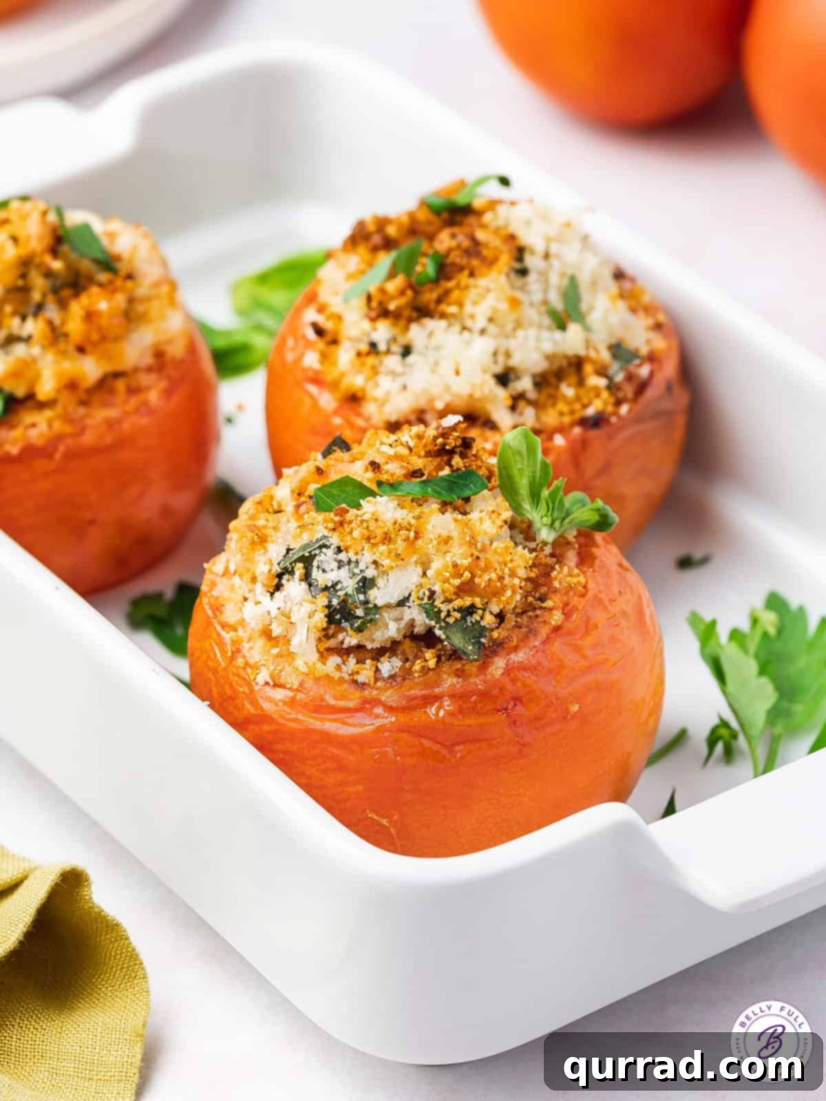 Three roasted stuffed tomatoes beautifully arranged in a white serving dish, garnished with fresh herbs.