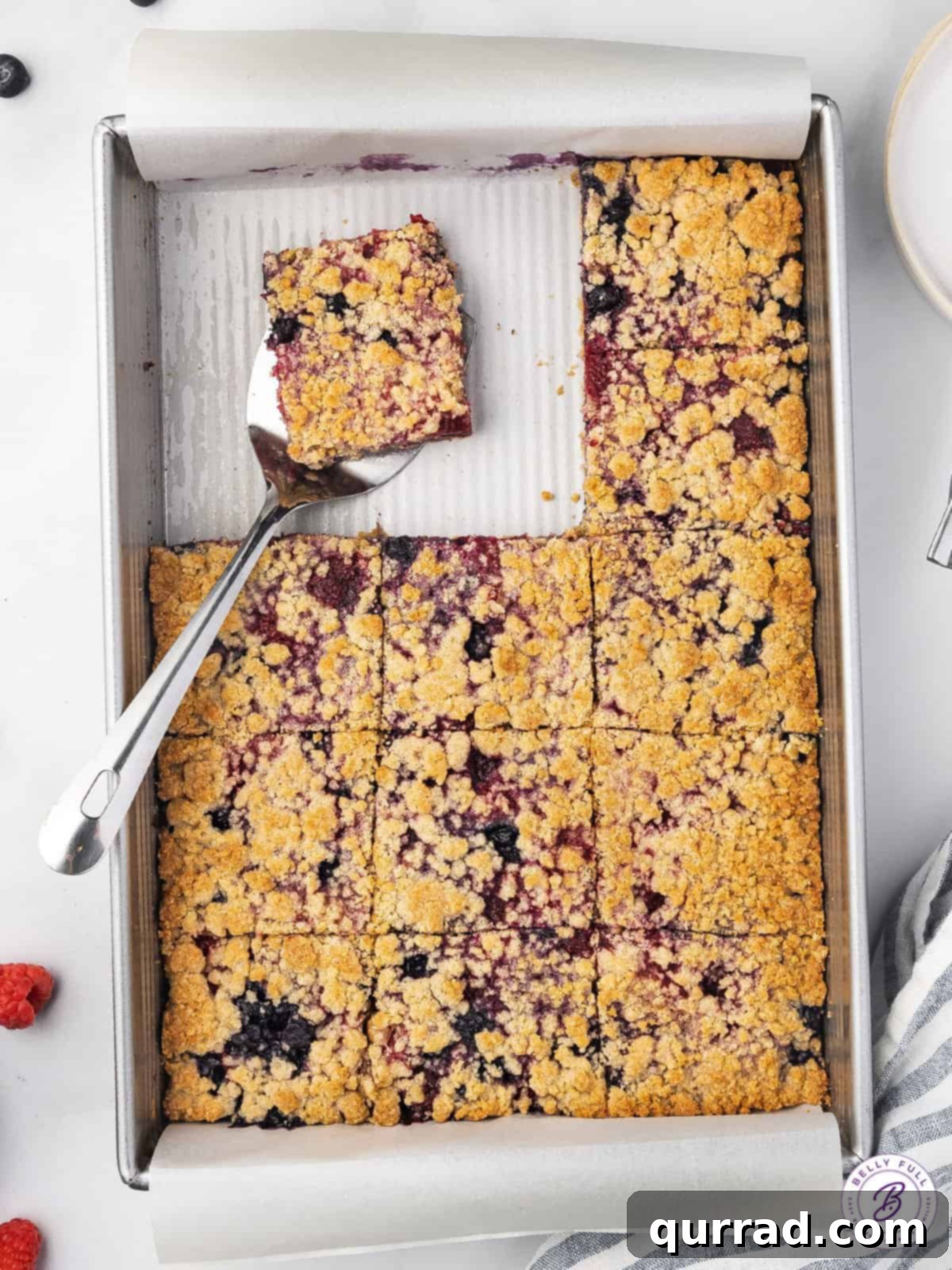 Overhead view of a pan of berry crumb bars, with one bar being lifted by a spatula