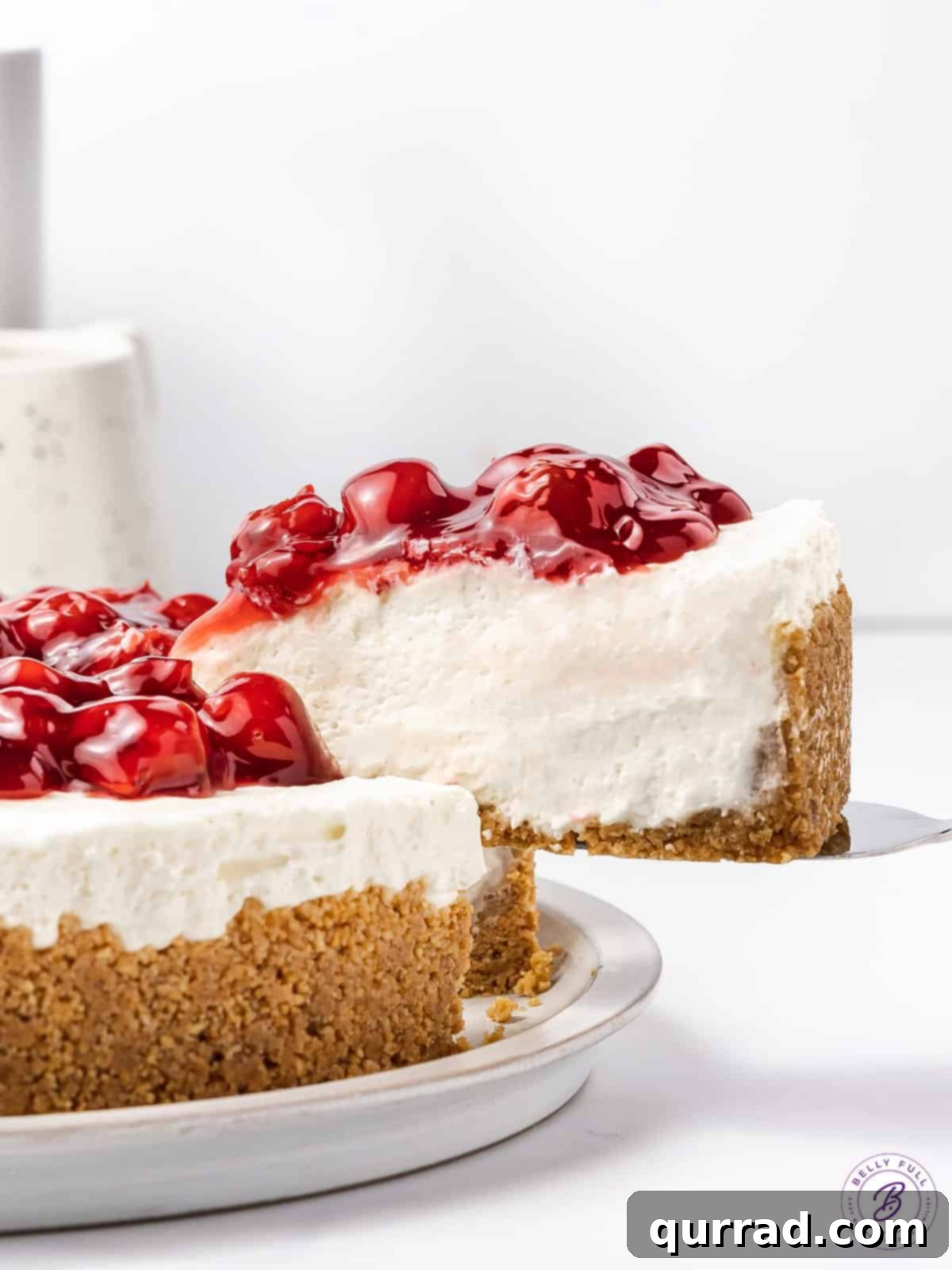With a tangy filling, graham cracker crust and cherry pie topping, this No Bake Cherry Cheesecake is the perfect balance of tart & sweet. Two perfectly sliced pieces of no-bake cherry cheesecake, each on a white plate, ready to be served and enjoyed.