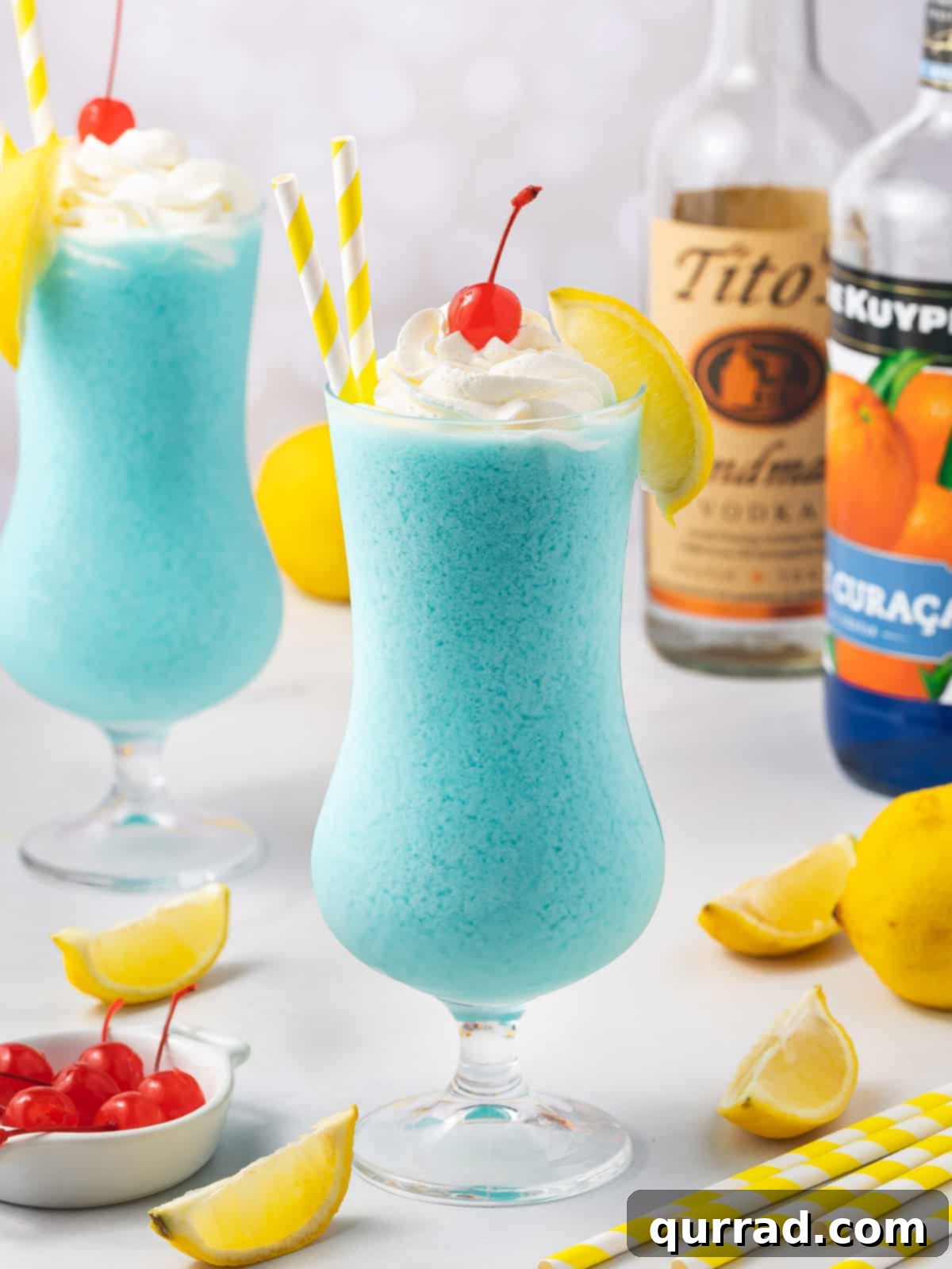 A vibrant Frozen Blue Lagoon cocktail, garnished with a cloud of whipped cream and a bright red maraschino cherry, ready to be enjoyed on a hot day.