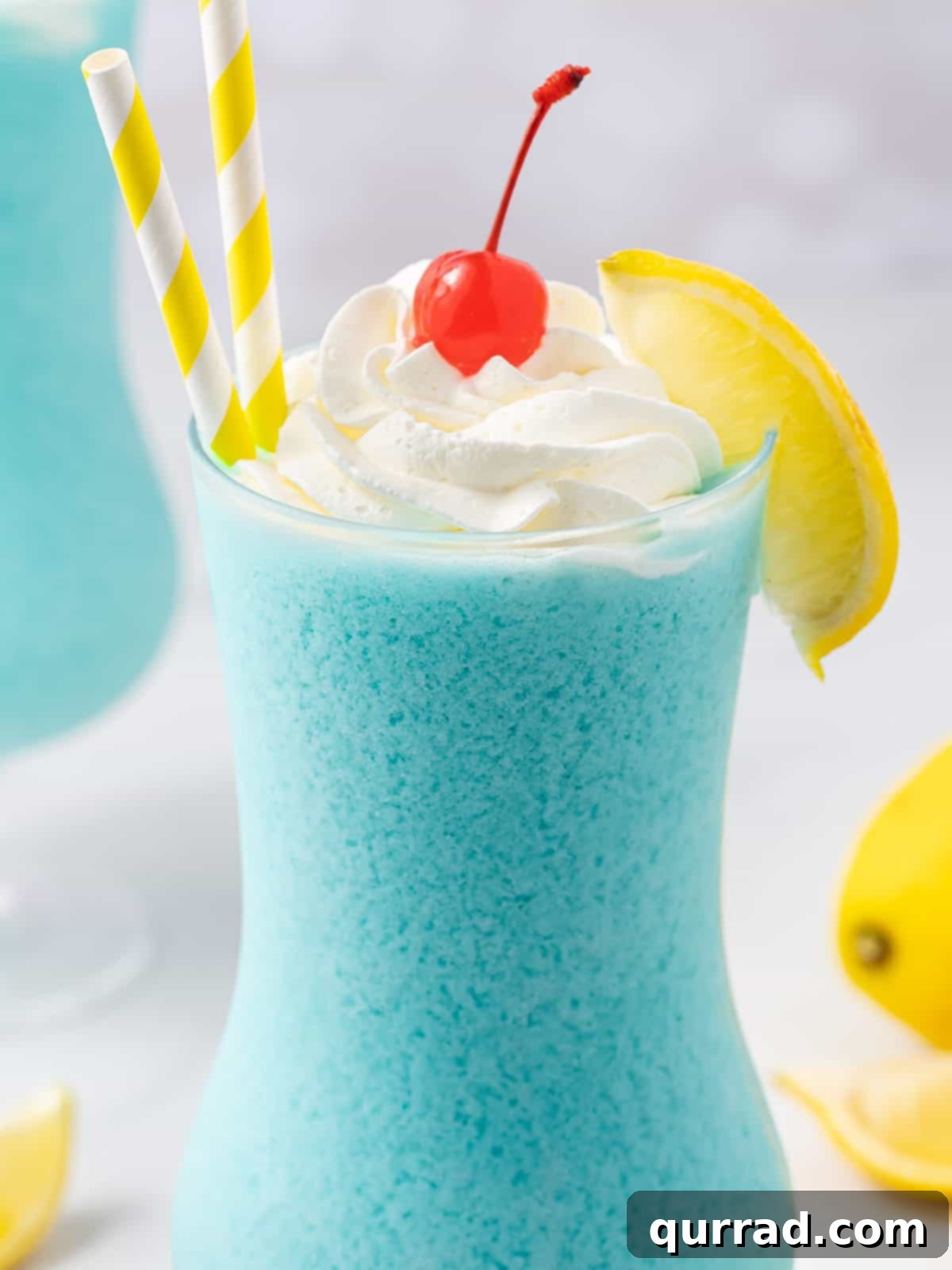 A close-up shot of a Frozen Blue Lagoon cocktail, emphasizing its creamy texture and rich blue color, with garnishes of whipped cream and a cherry.