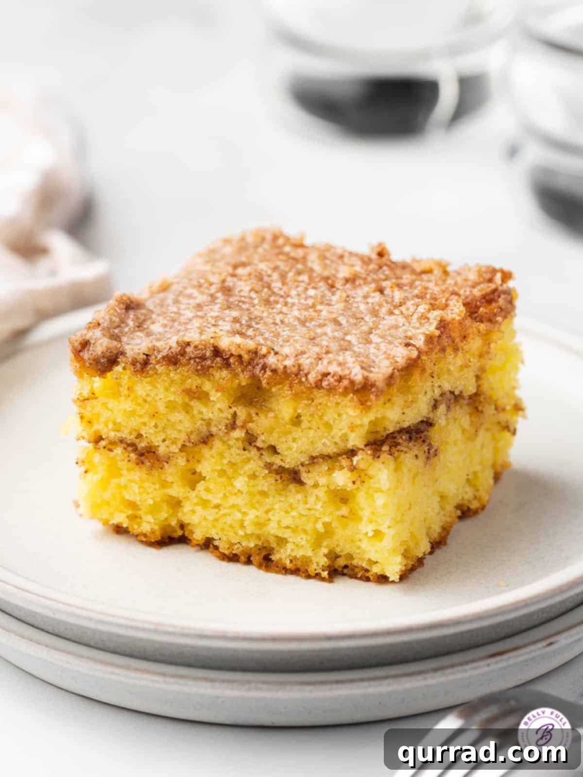 Square slice of honey bun cake on a white plate, highlighting its moist texture and cinnamon swirl.
