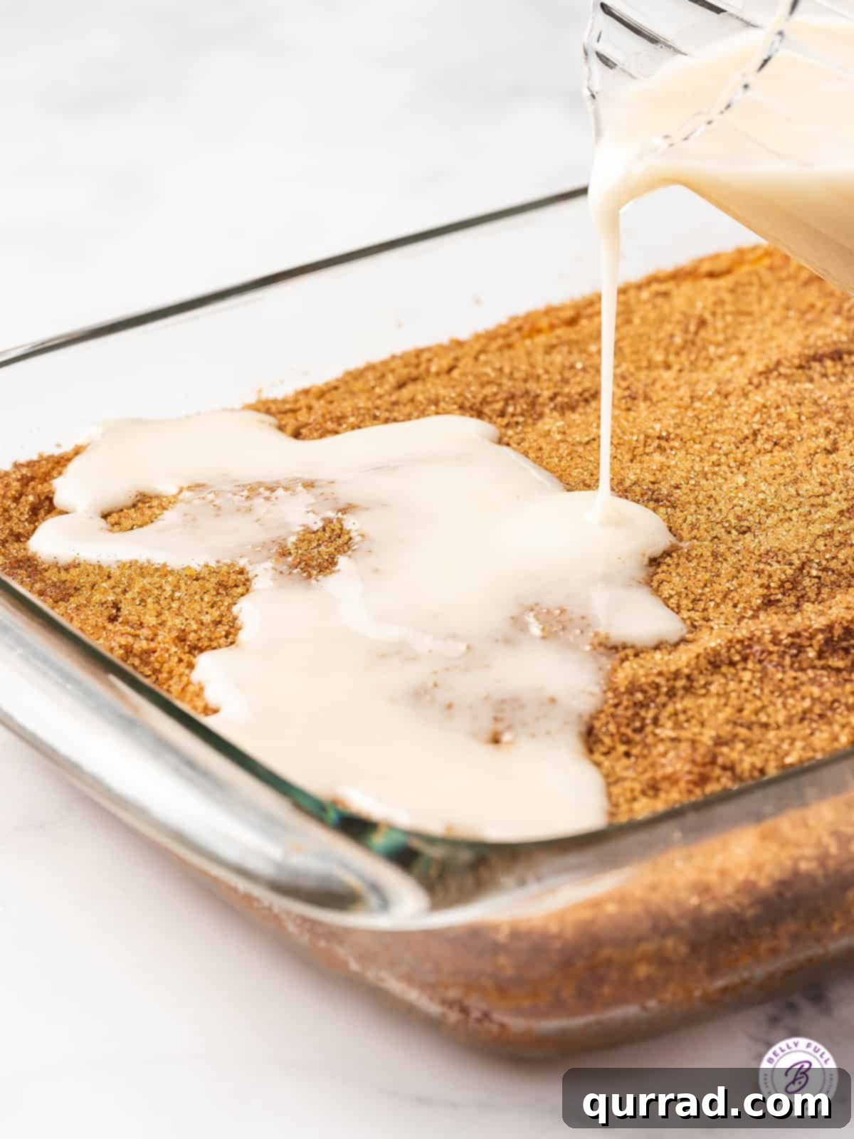 Vanilla glaze being generously poured over a warm, baked honey bun cake.