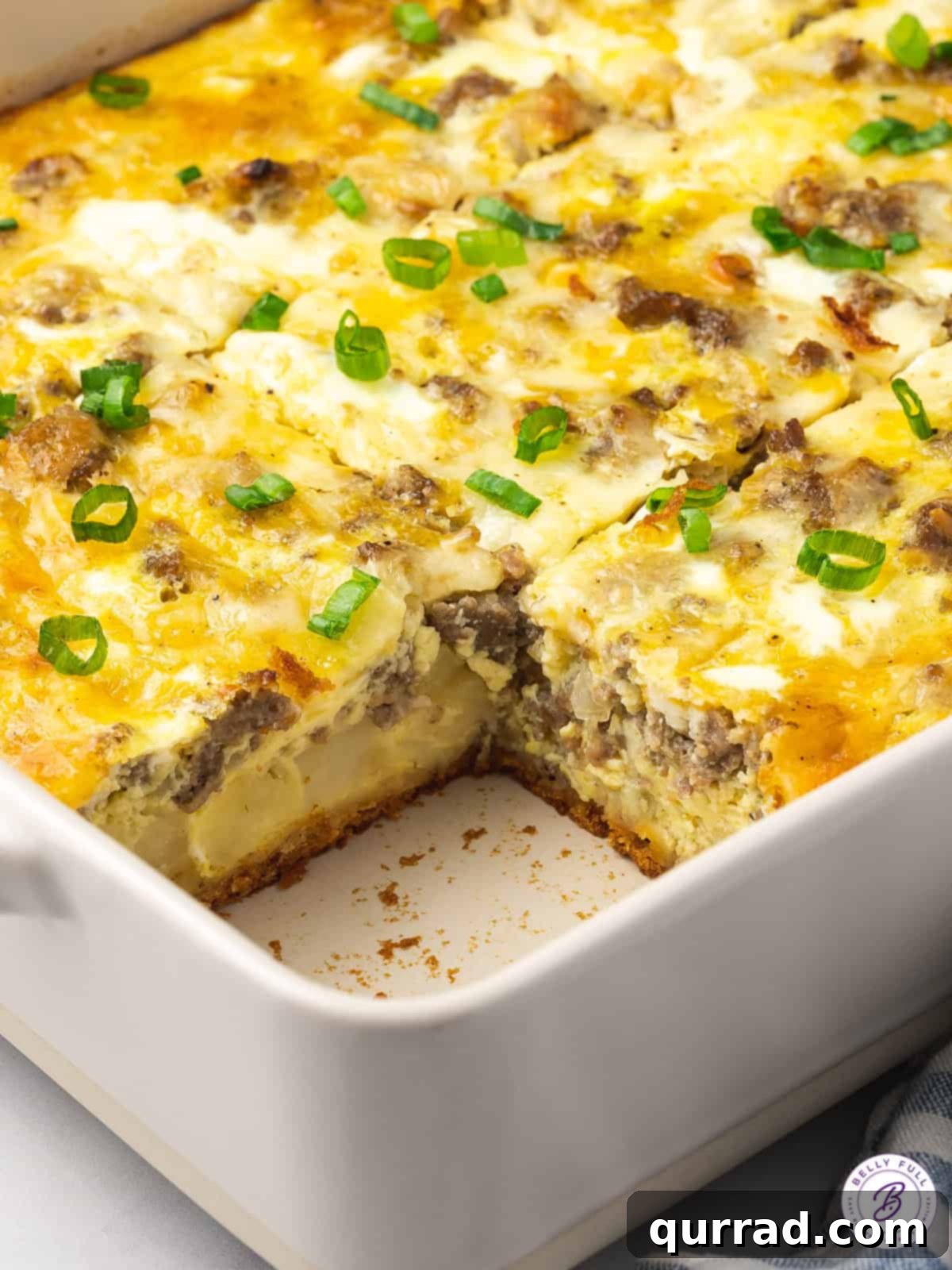 A portion of crescent roll egg bake is missing, showing its golden crust and richly layered interior of eggs, sausage, and hash browns. Angled view of a crescent roll egg bake with a slice removed, revealing the delicious layers inside.