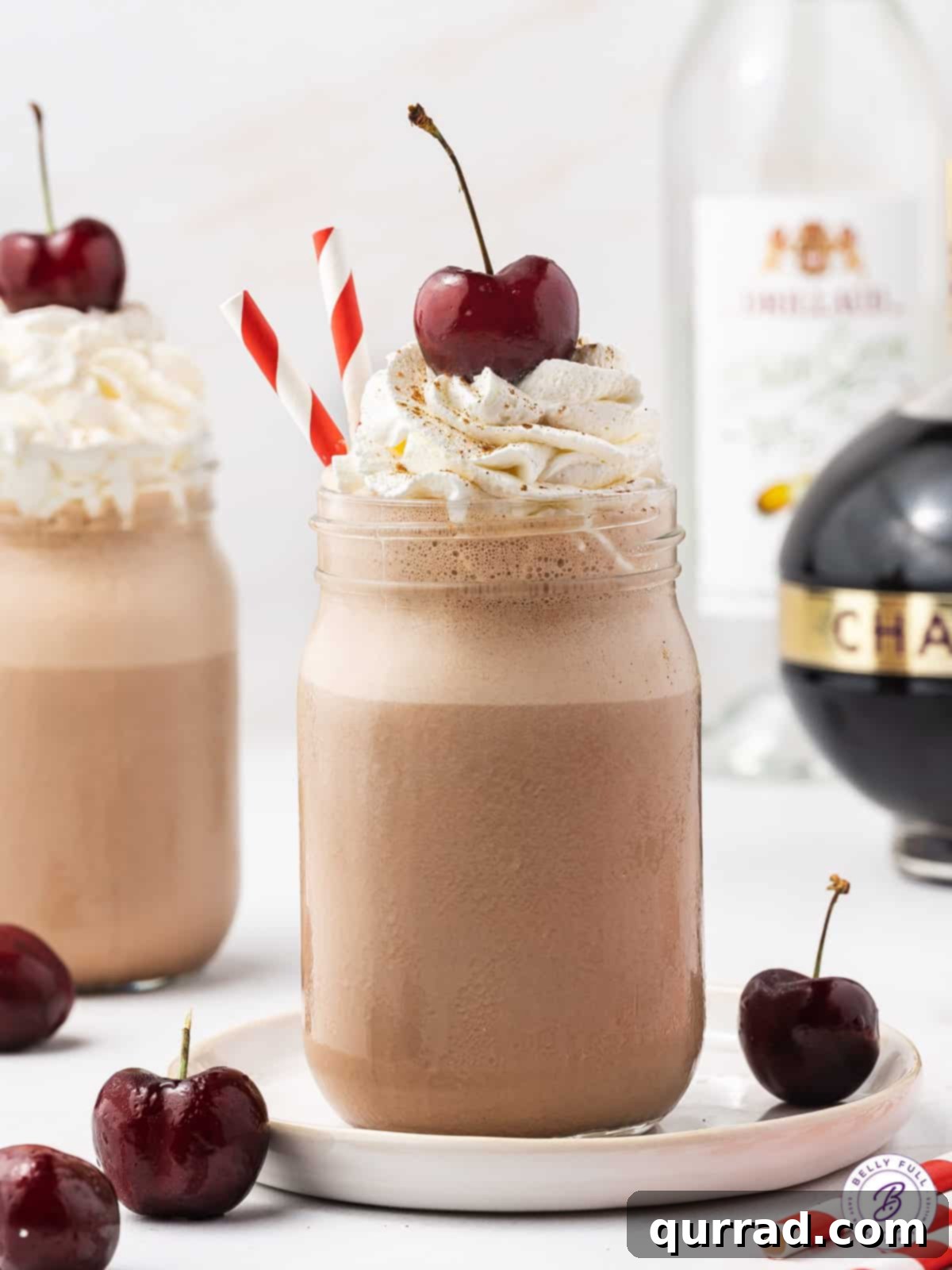 Savor the ultimate adult dessert: A Boozy Black Forest Milkshake, masterfully blended with vodka, creme de cacao, Chambord, and rich chocolate ice cream for unparalleled decadence. A Boozy Black Forest Milkshake in a tall glass, beautifully garnished with a swirl of whipped cream and a glistening dark cherry, set against a rustic background.