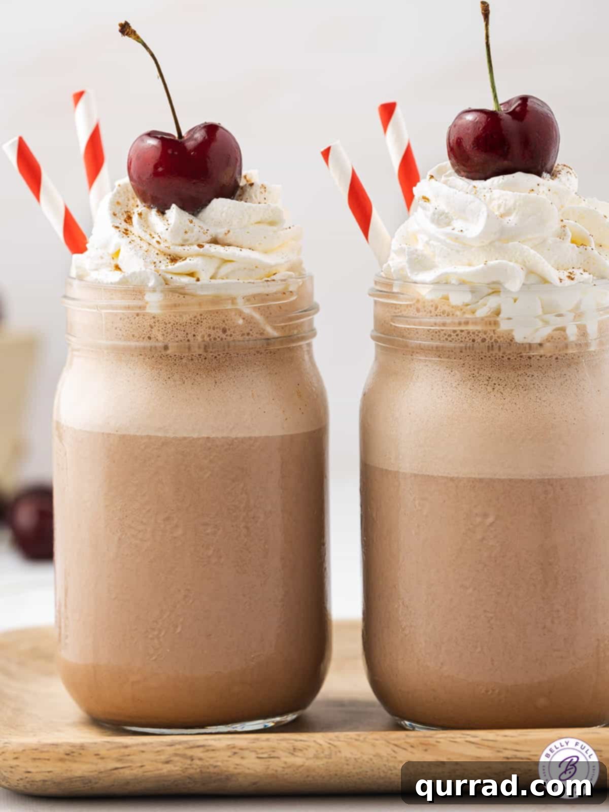 Share the perfect indulgence! Two Boozy Black Forest Milkshakes, ready to be enjoyed as a delightful dessert or a spirited cocktail for two. Two glasses of Boozy Black Forest Milkshakes, artfully topped with whipped cream and cherries, creating an inviting scene against a subtly dark background.