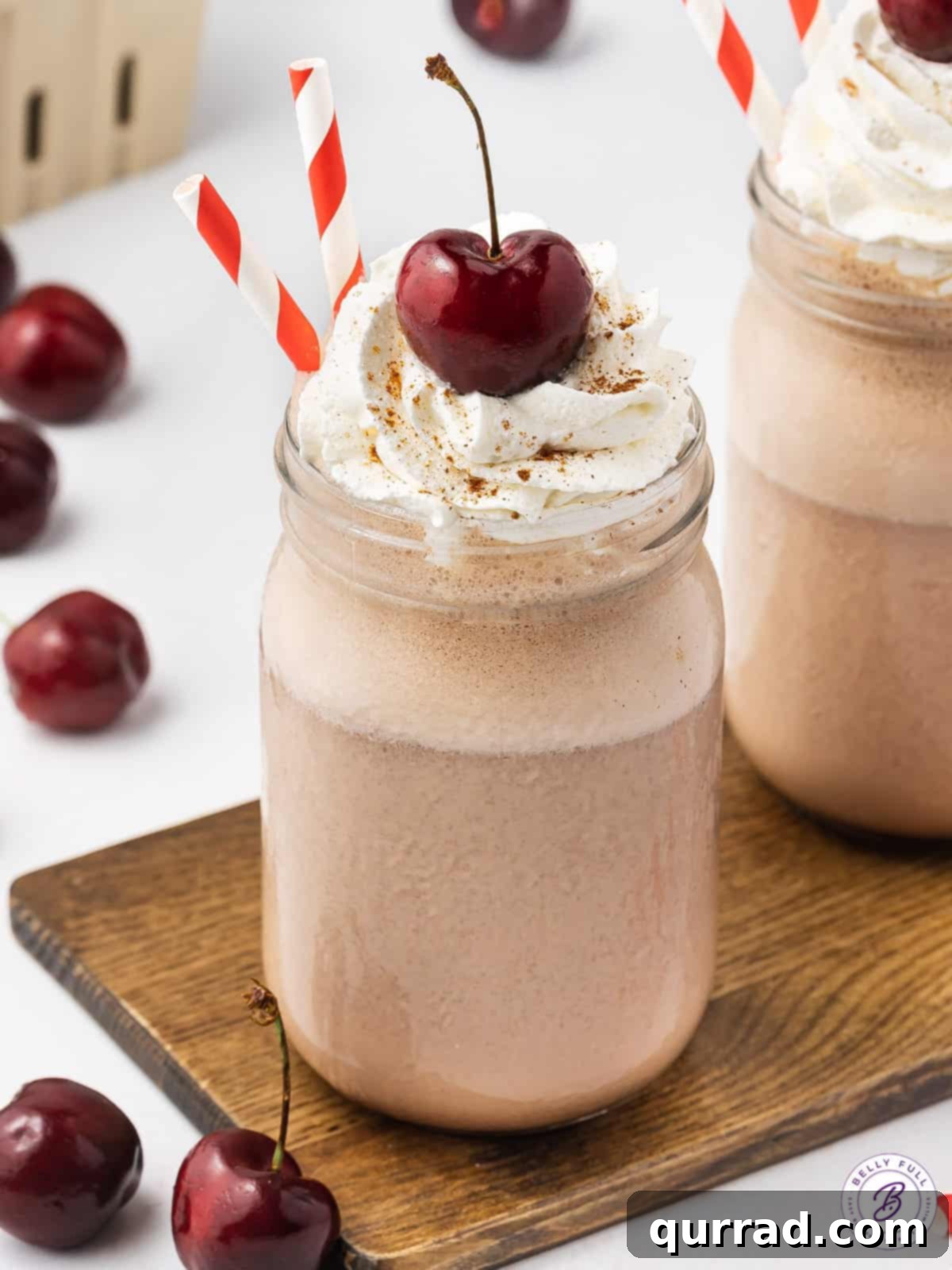 Pure indulgence captured: A Boozy Black Forest Milkshake, perfectly garnished and ready to be enjoyed as a decadent and spirited dessert. A detailed close-up of a single Boozy Black Forest Milkshake, exquisitely topped with a swirl of fluffy whipped cream and a gleaming dark cherry, promising pure indulgence.