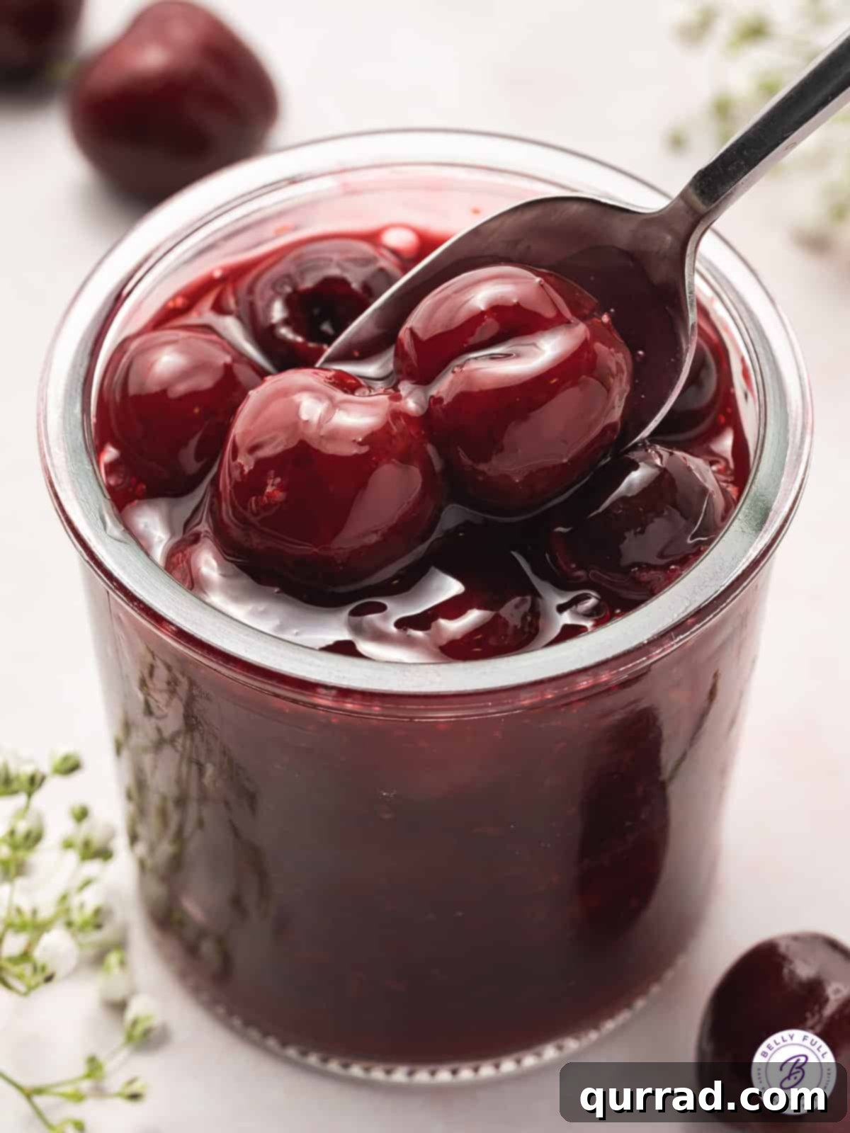 A spoon in a jar of homemade cherry pie filling, showcasing its rich red color and plump cherries.